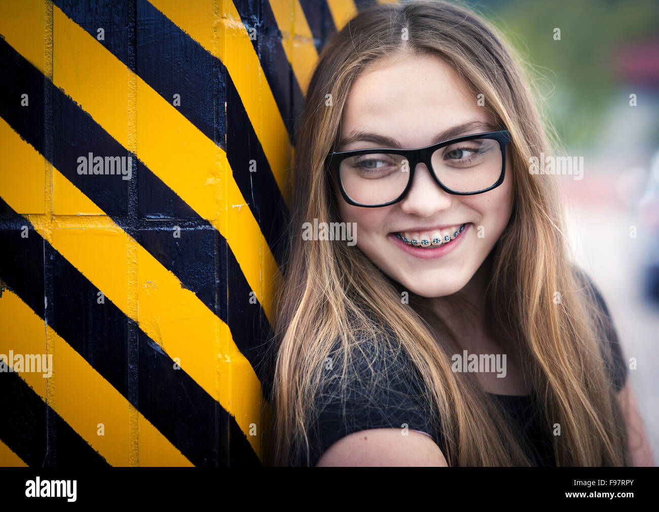 Portrait of smiling teenage hipster girl standing by the black and yellow striped warning wall Stock Photo