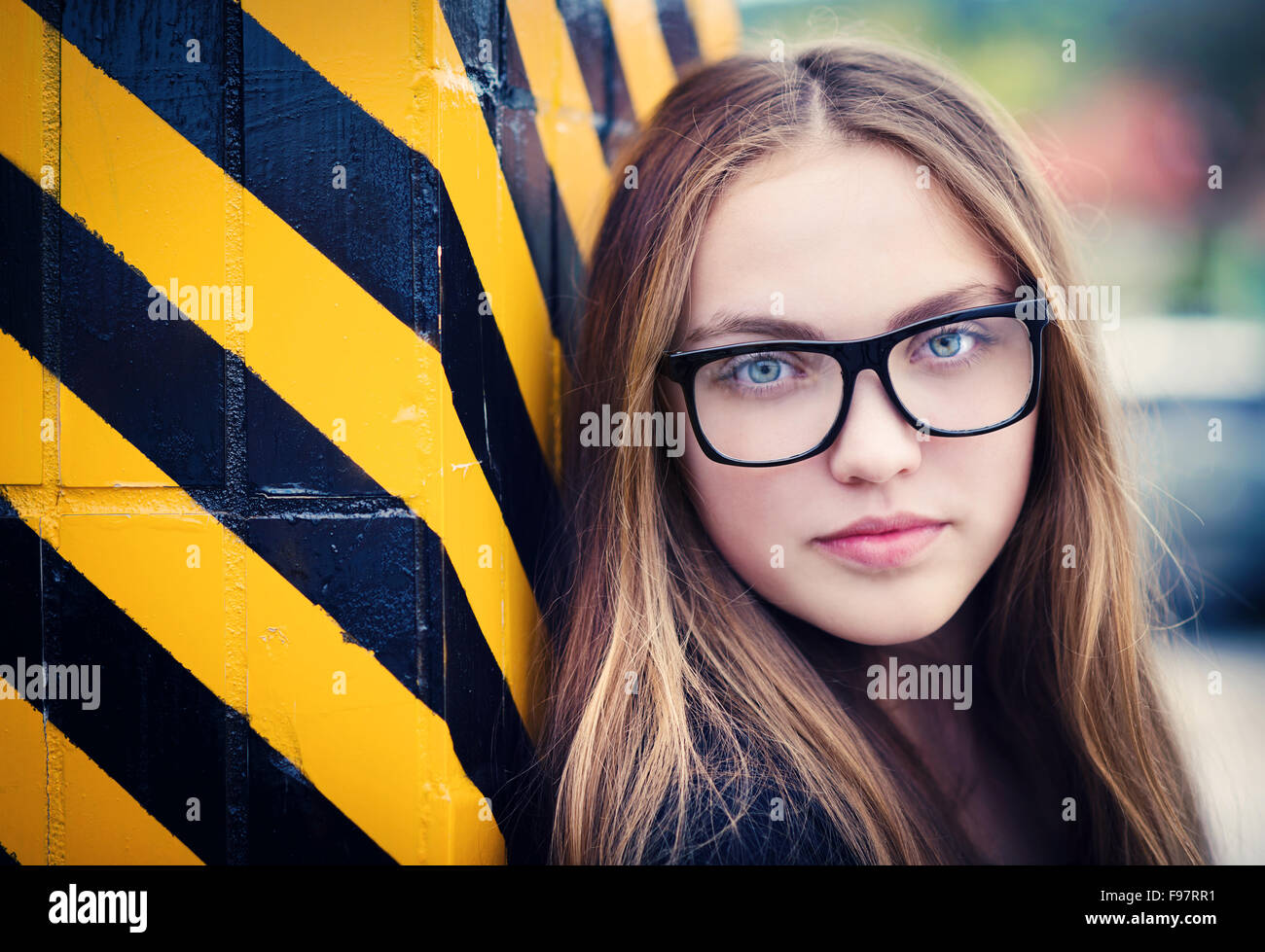 Portrait of sad teenage hipster girl standing by the black and yellow striped warning wall Stock Photo