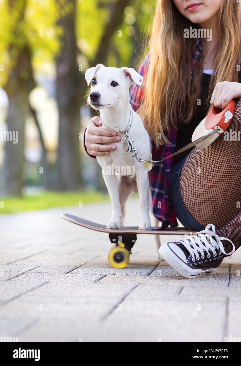 Close-up of legs of teenage girl on skateboard with her dog Stock Photo
