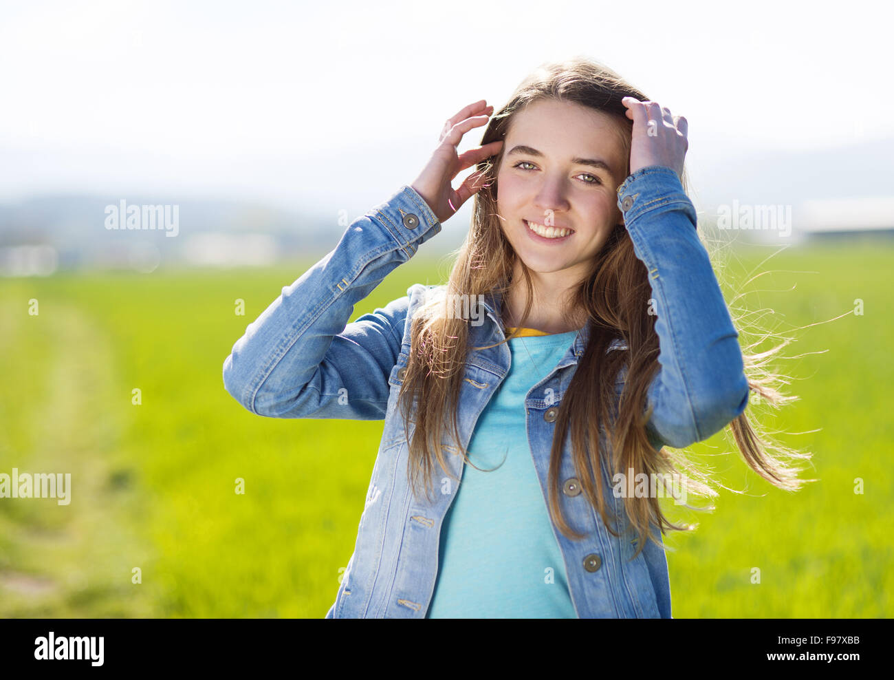 Happy young girl in blue jeans jacket enjoying free time in green field