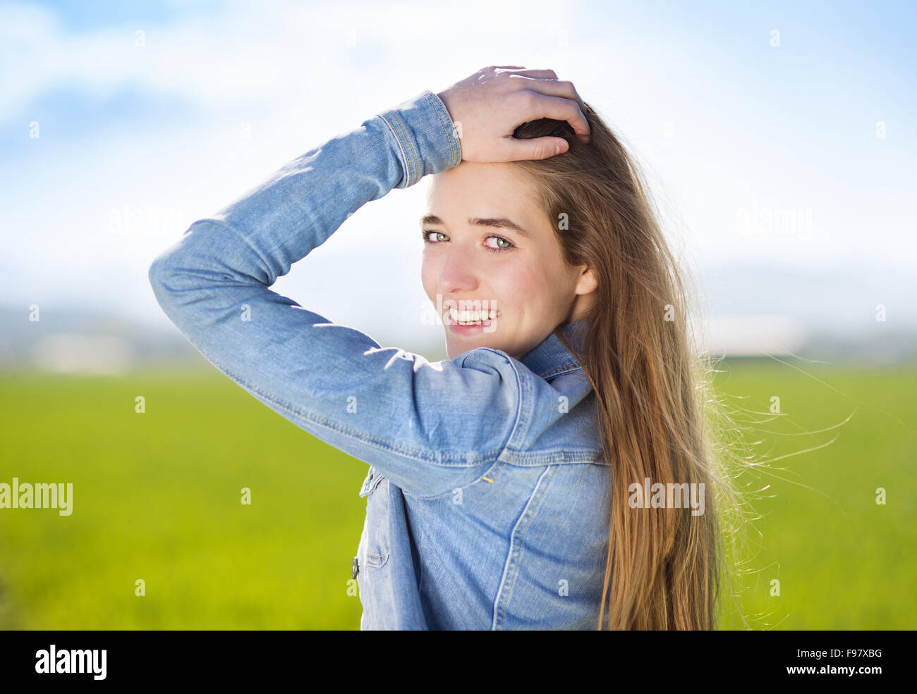 Happy young girl in blue jeans jacket enjoying free time in green field