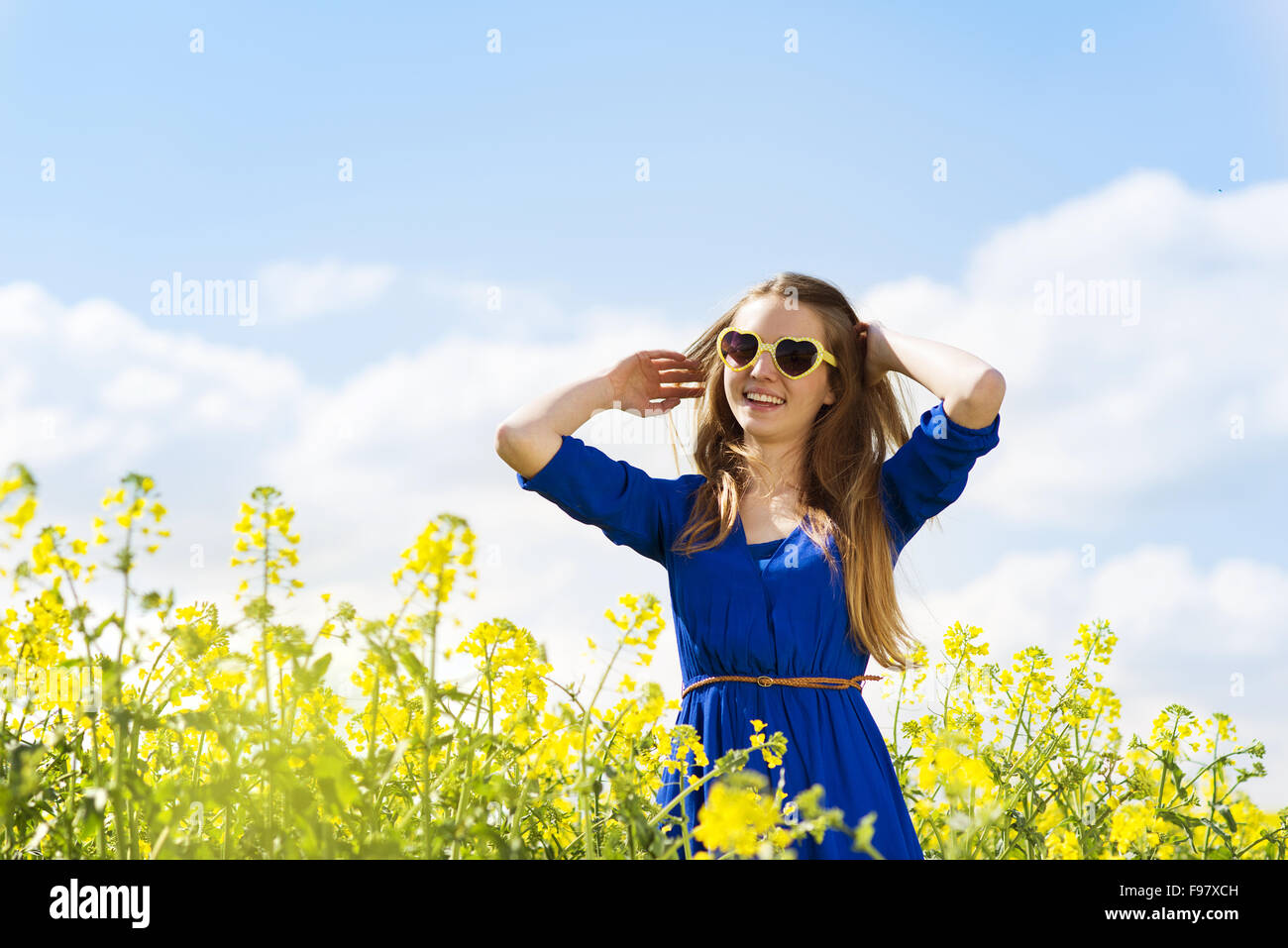 Happy young girl in blue dres nad sunglasses enjoying free time in yellow colza field Stock Photo