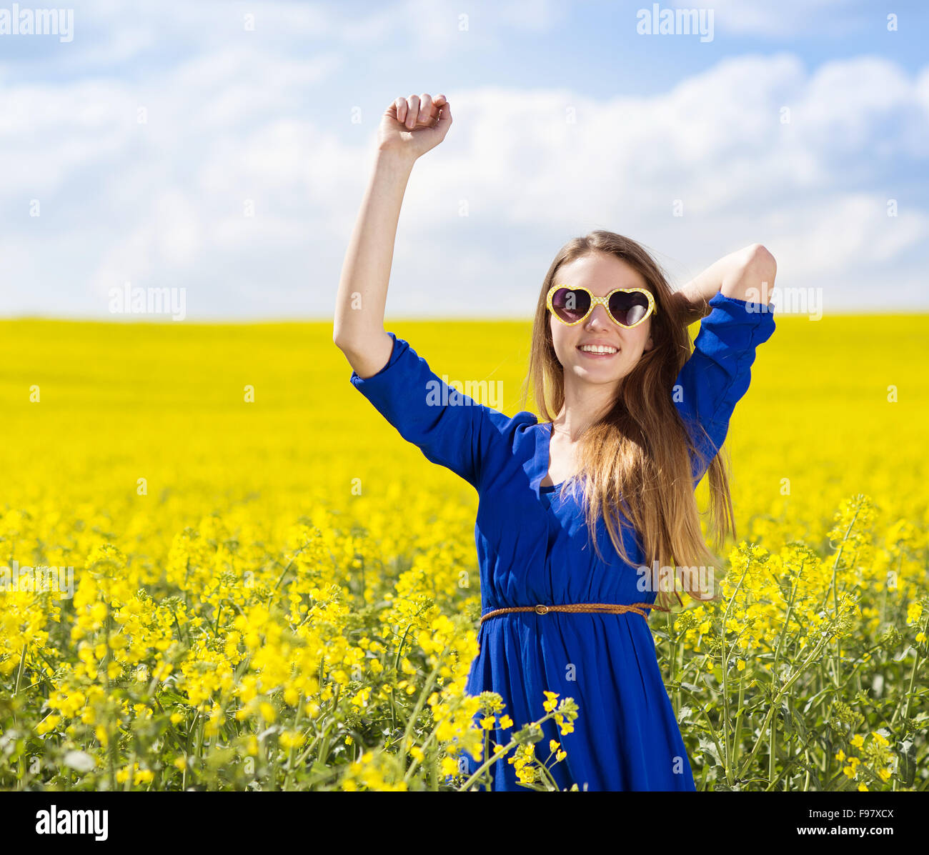 Happy young girl in blue dres nad sunglasses enjoying free time in yellow colza field Stock Photo