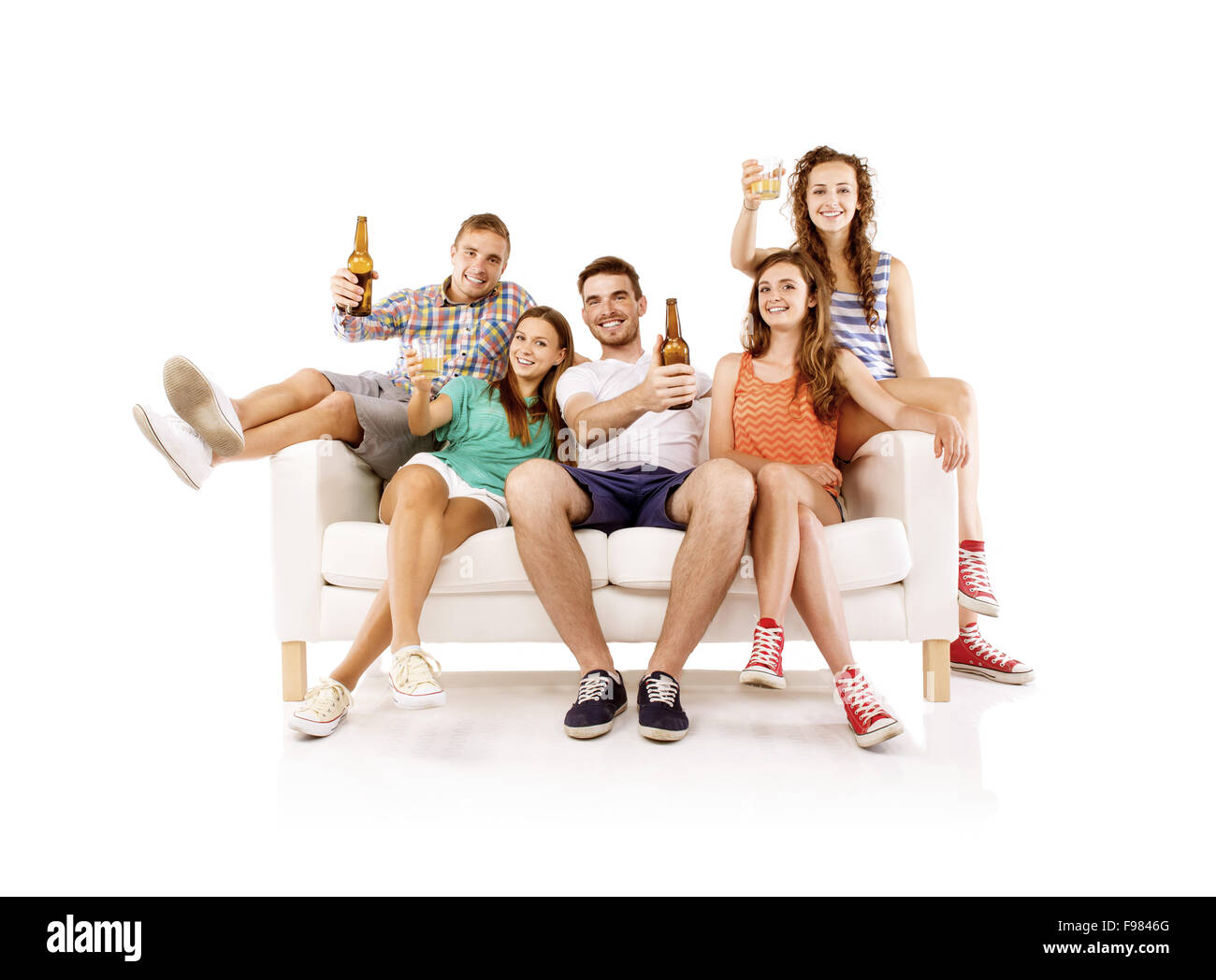 Group of happy young people sitting on sofa with bottled drinks, isolated on white background. Best friends Stock Photo