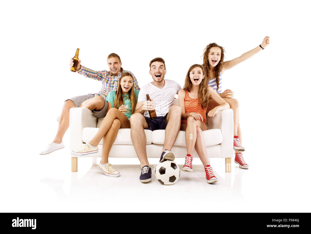 Group of happy young people sitting on sofa and holding soccer ball and bottled drinks, isolated on white background. Best frien Stock Photo