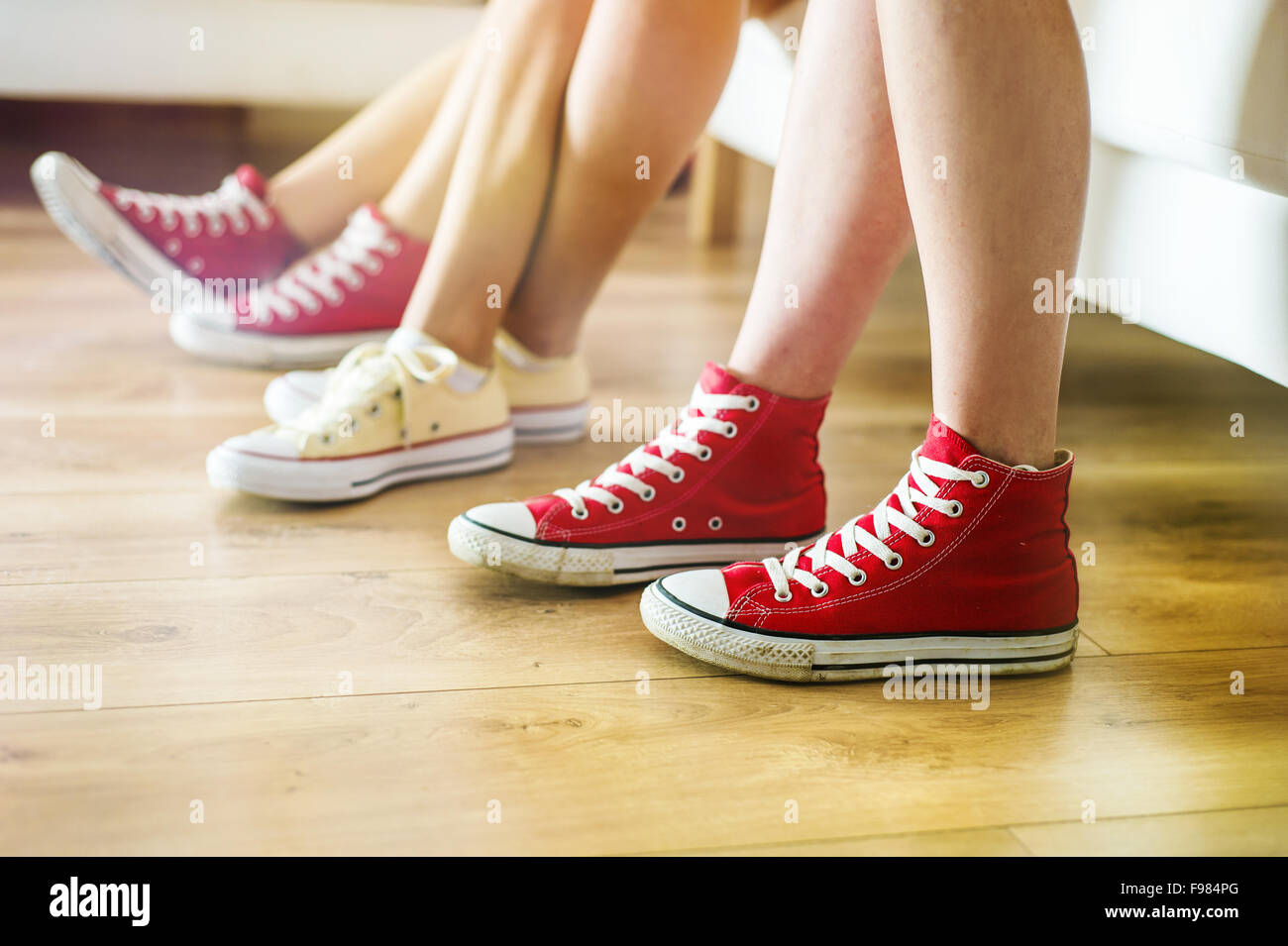 Three young girls sitting on sofa, closup on legs and sneakers Stock Photo