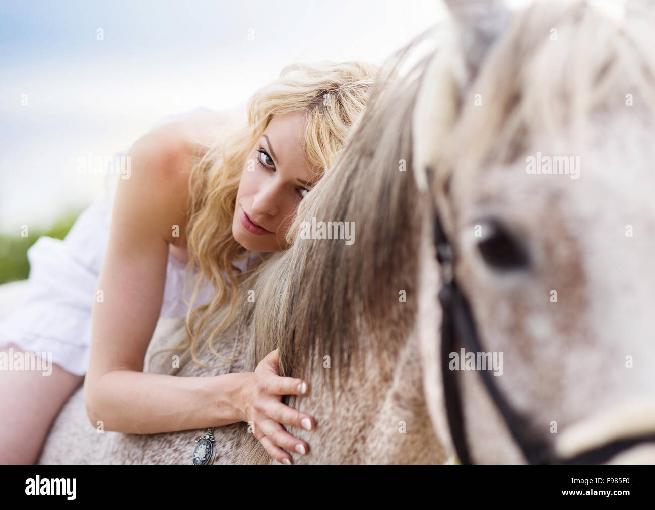 Woman in white dress walking with horse in green countryside Stock