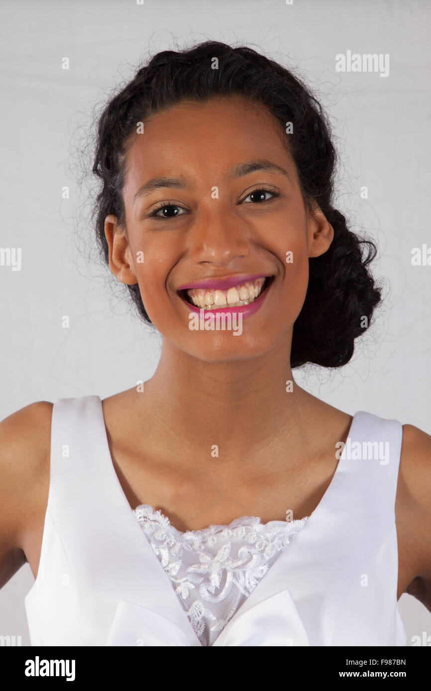 Pretty black woman in a white wedding type of dress, smiling for joy Stock Photo