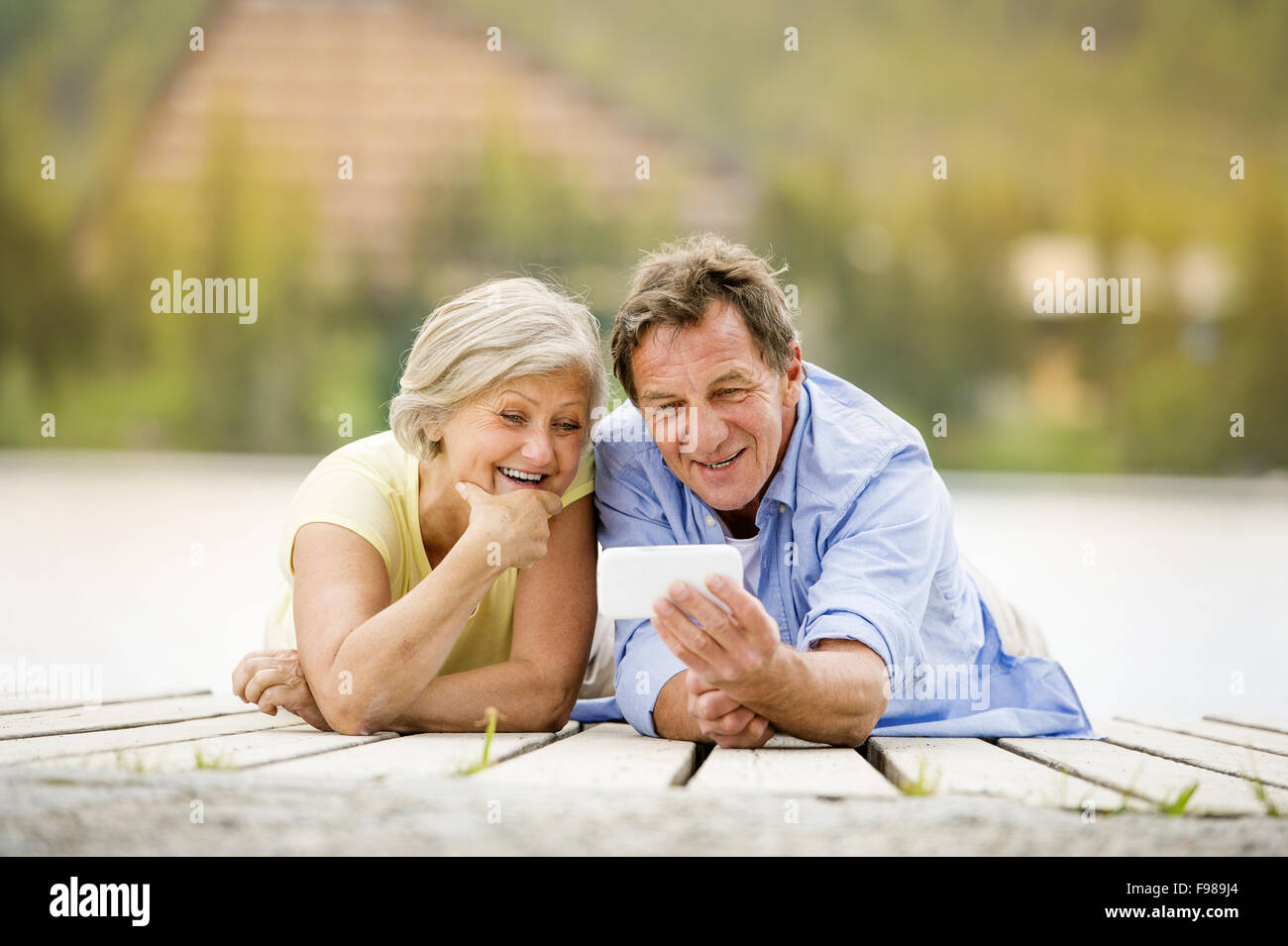 Senior couple lying down and taking selfie on pier Stock Photo