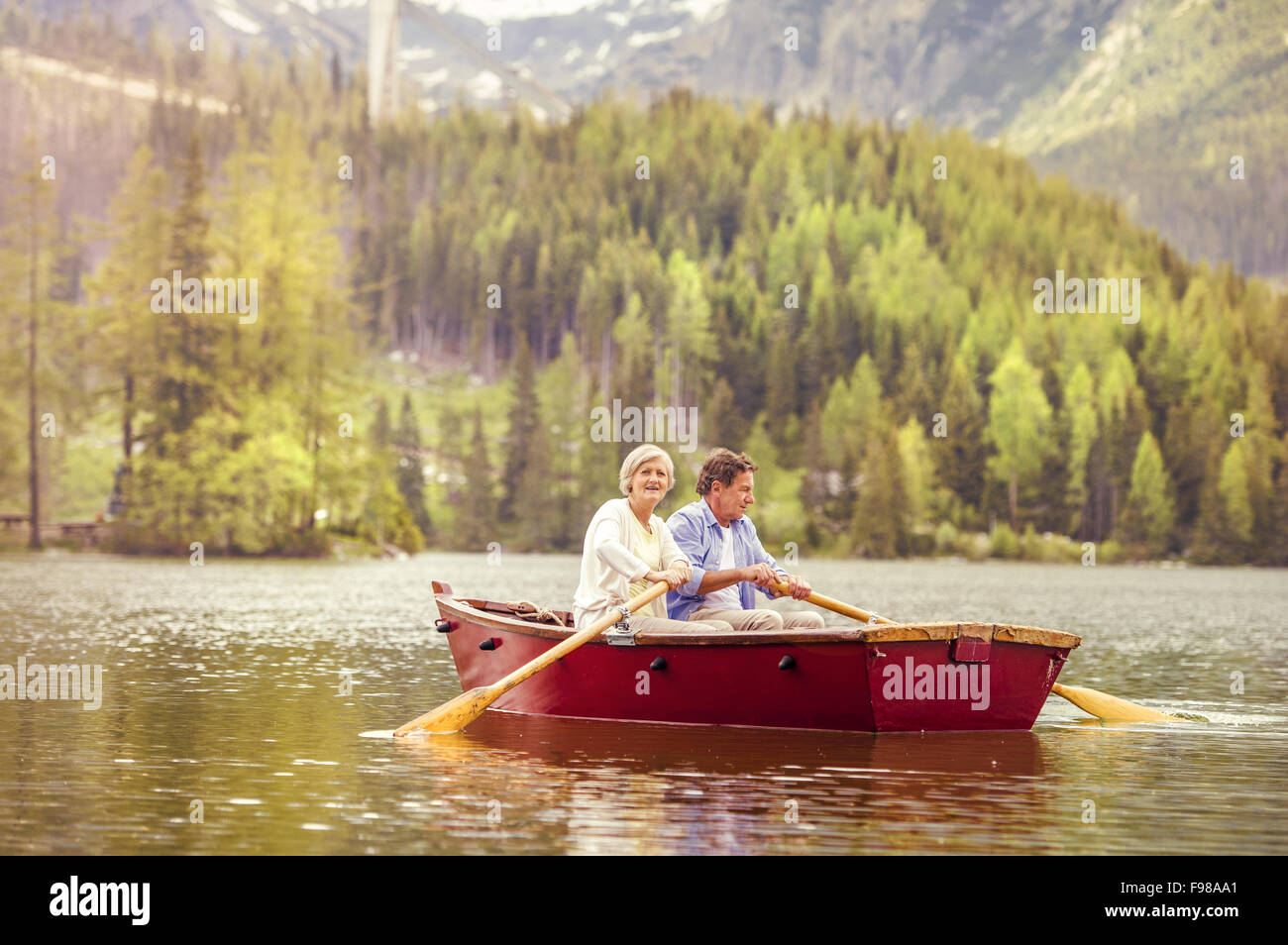 Senior couple paddling on boat with mountains in background Stock Photo