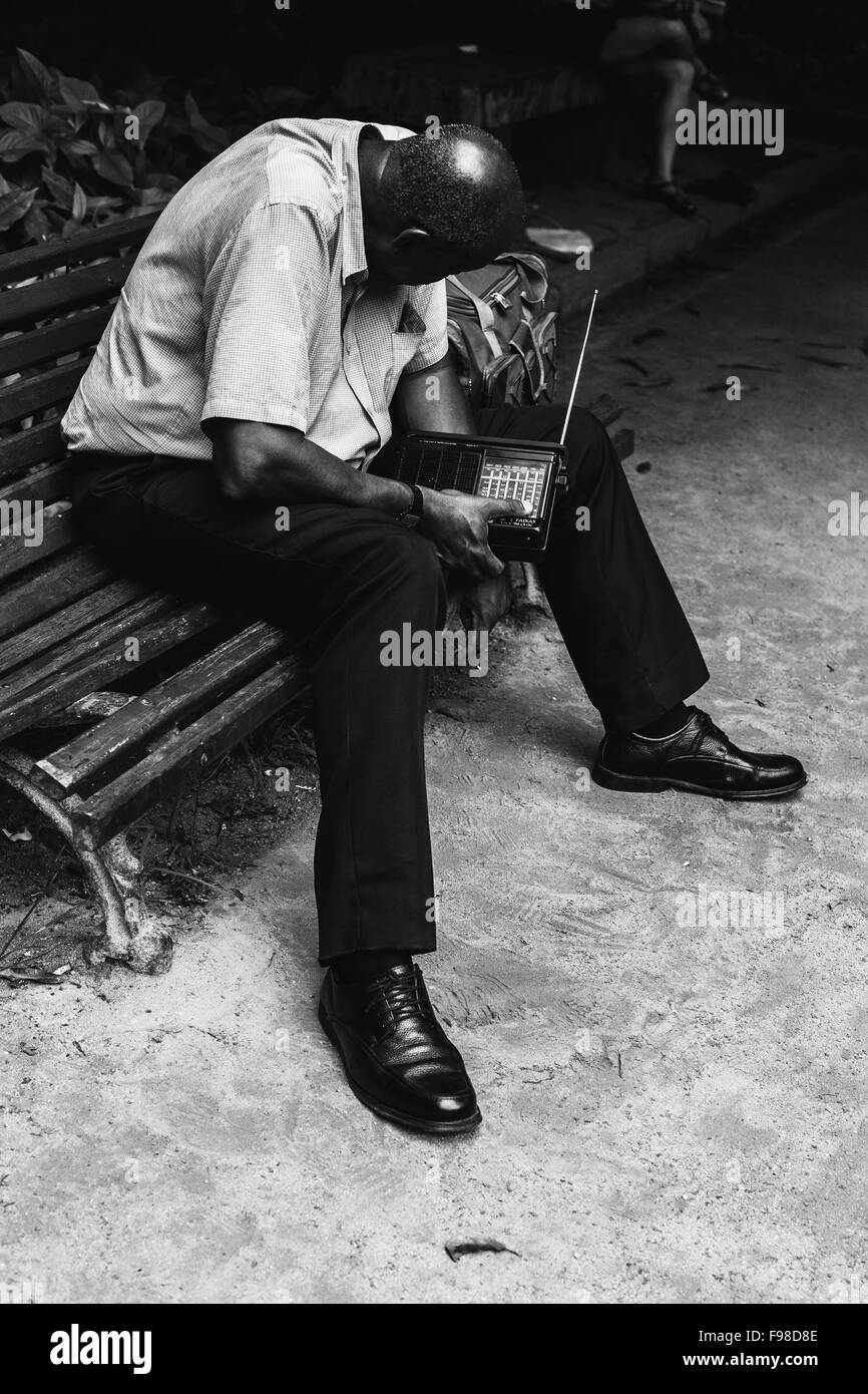 an older black man sits on a bench listening to a radio Stock Photo