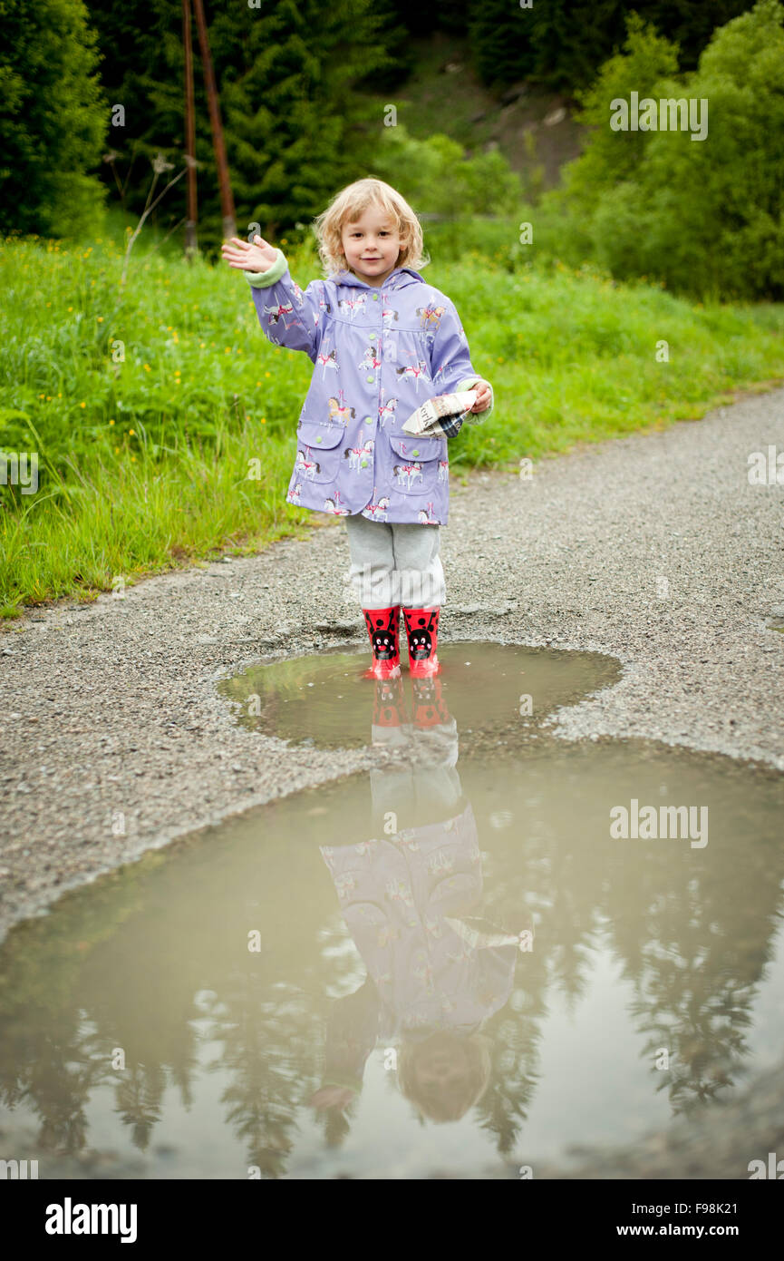 Little girl playing in a water puddle with a paper boat Stock Photo - Alamy