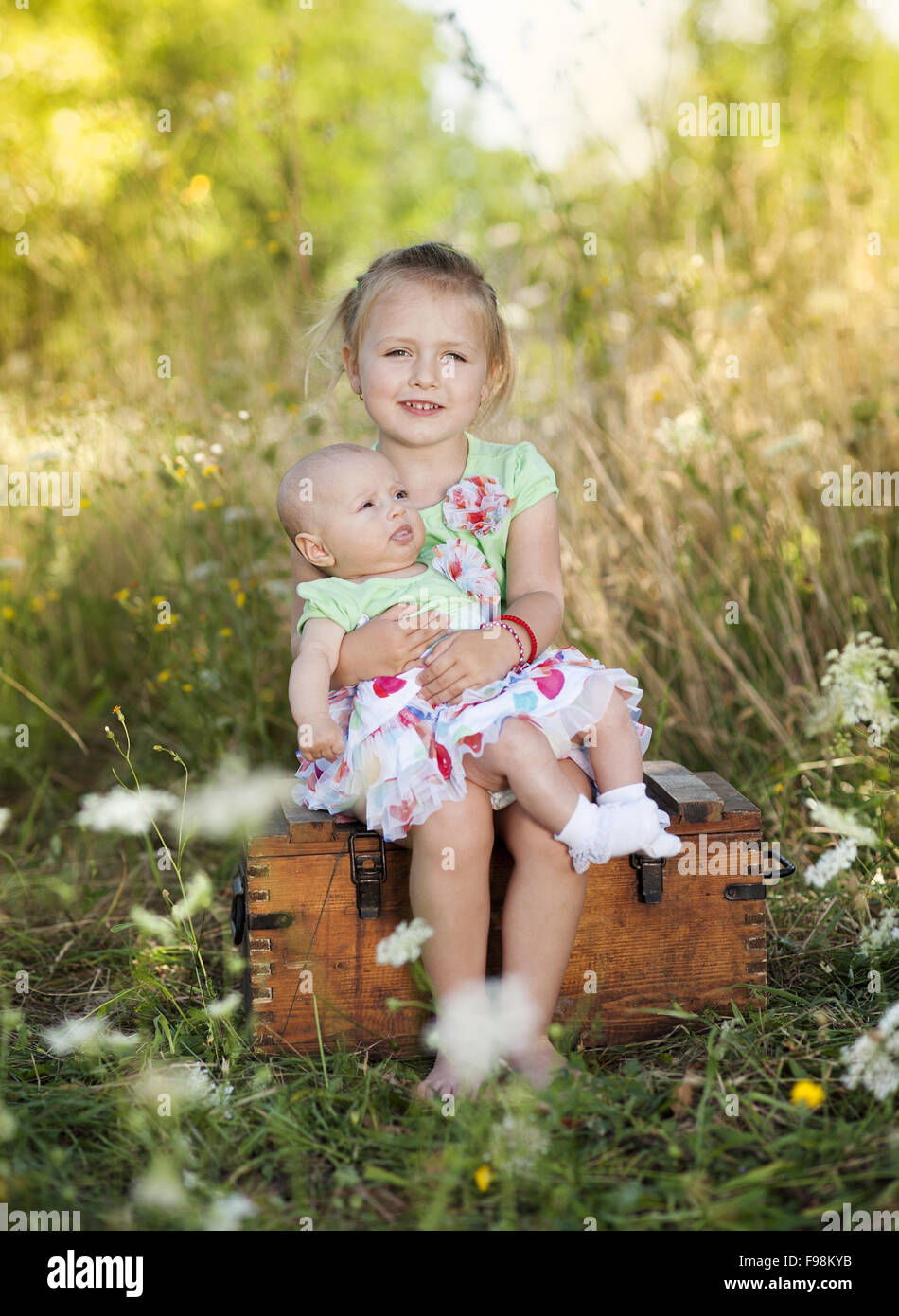 Summer outdoor portrait of cute little girl holding her baby sister and