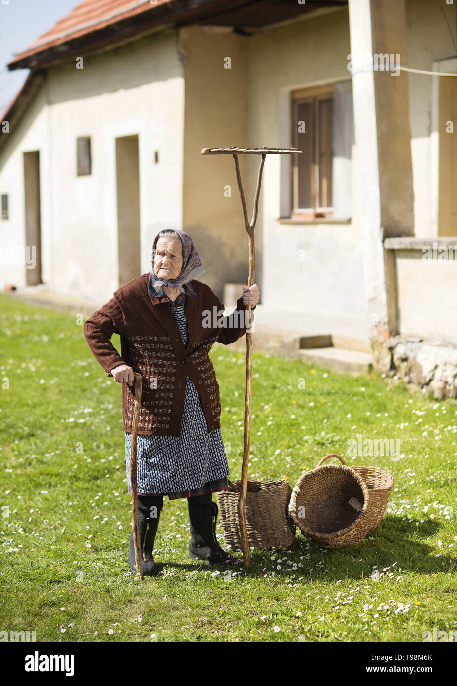 Very old woman in head scarf with garden tools in her back yard Stock