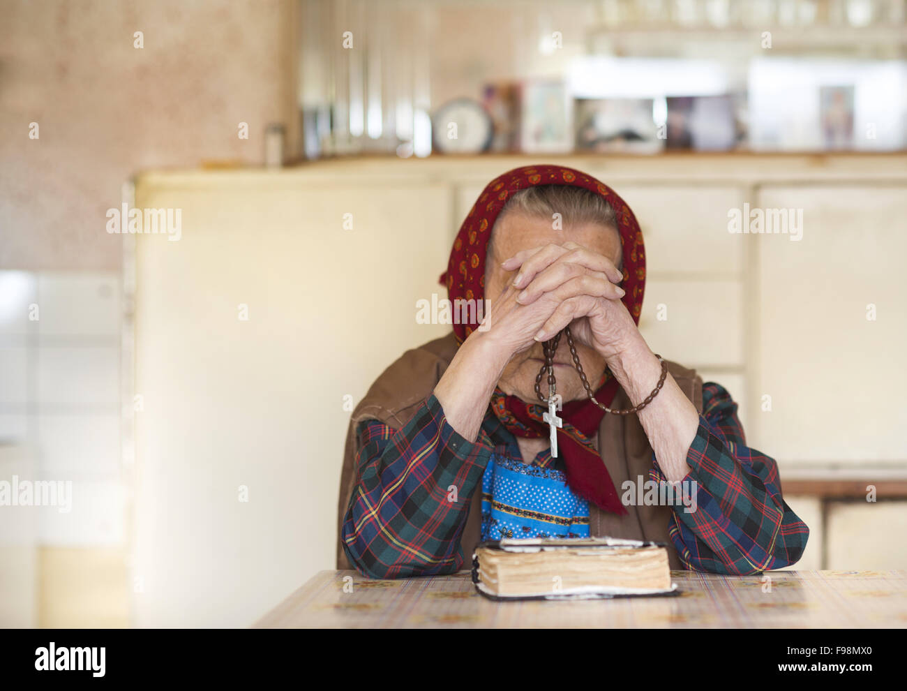 Very old woman wearing head scarf is praying in her country style kitchen Stock Photo