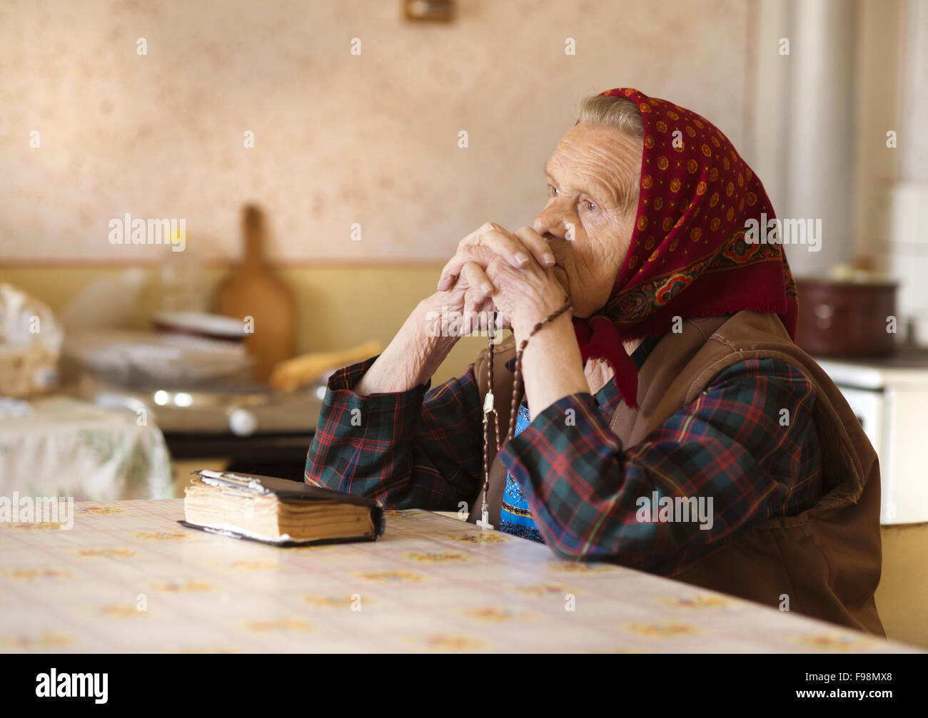 Very old woman wearing head scarf is praying in her country style kitchen Stock Photo