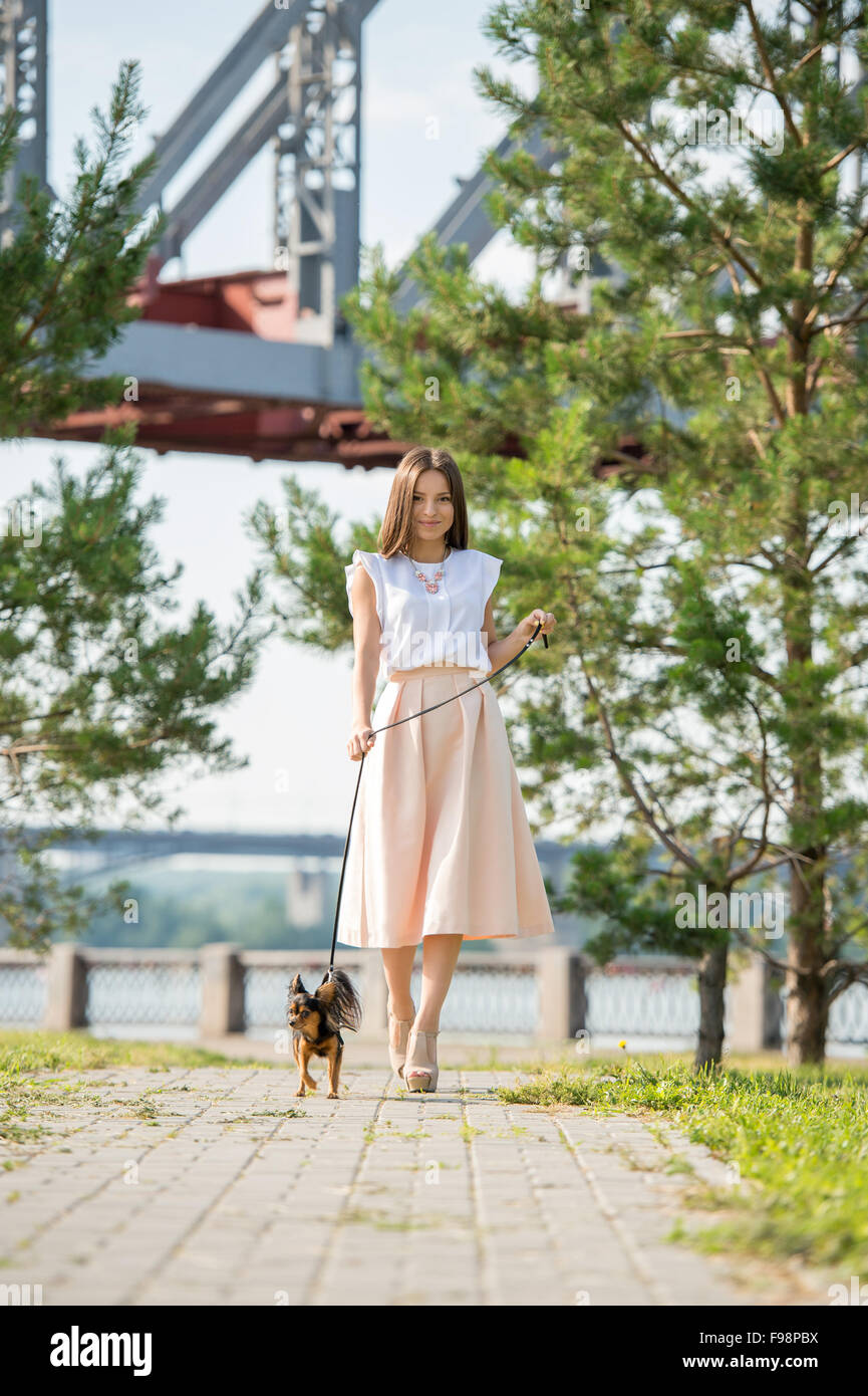 Young beautiful lady walking with her dog on lead in summer park Stock Photo