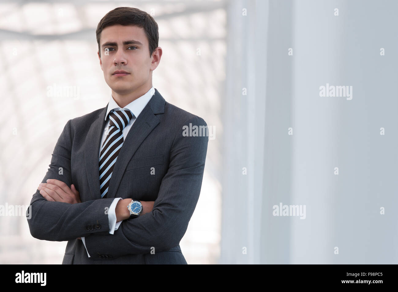 Portrait of handsome confident young businessman standing arms crossed ...