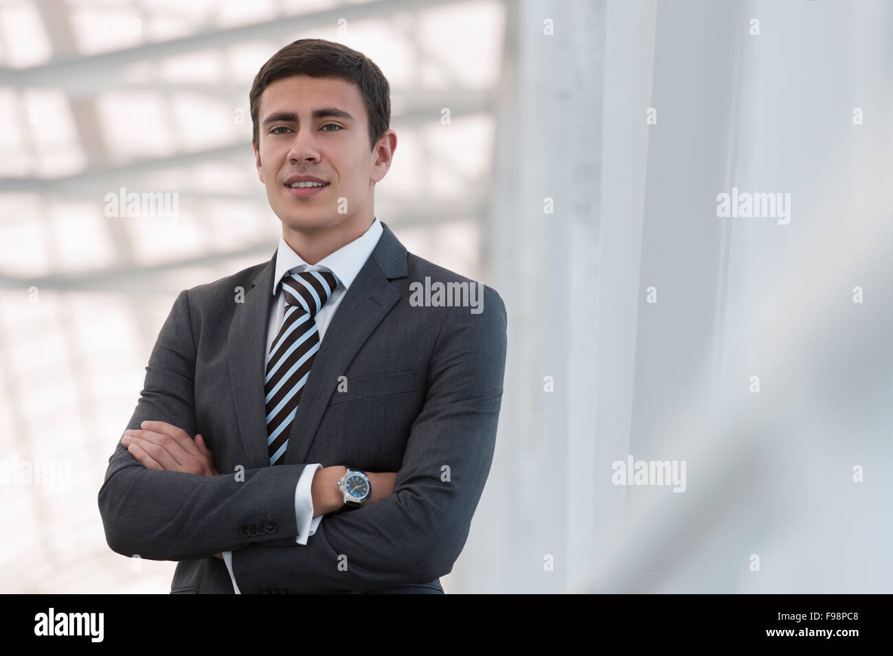 Portrait of handsome confident young businessman standing arms crossed ...