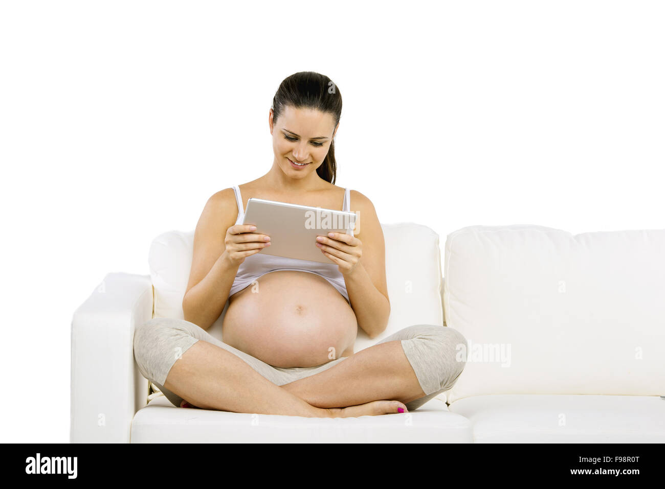 Studio portrait of pregnant woman with digital tablet sitting on sofa isolated on white background Stock Photo