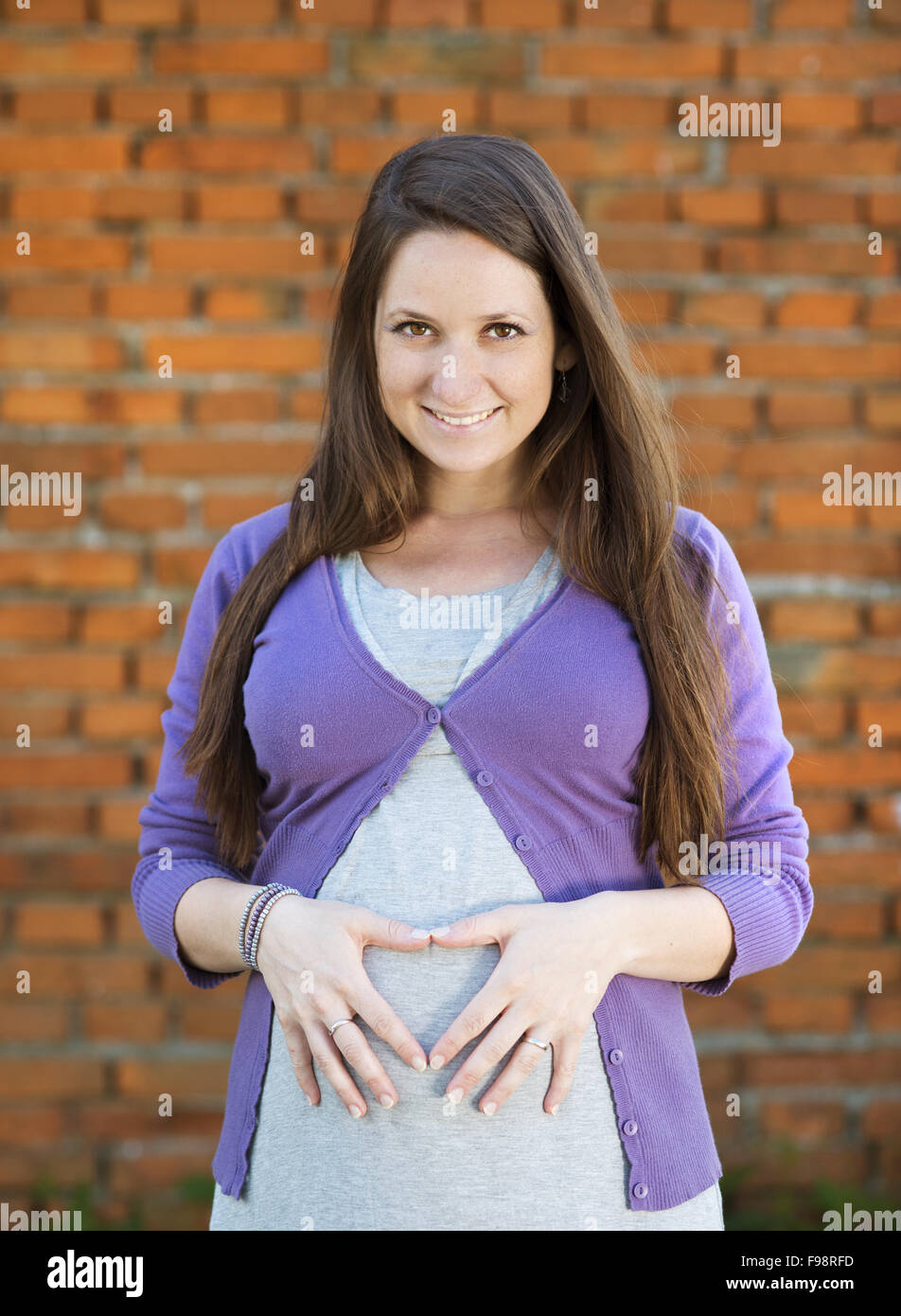 Outdoor Portrait Of Beautiful Pregnant Woman Holding Her Belly Brick Wall In Background Stock