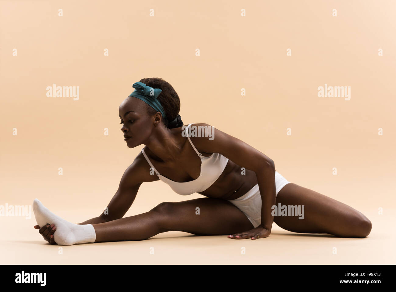 Portrait of young african woman doing stretching exercise on beige ...