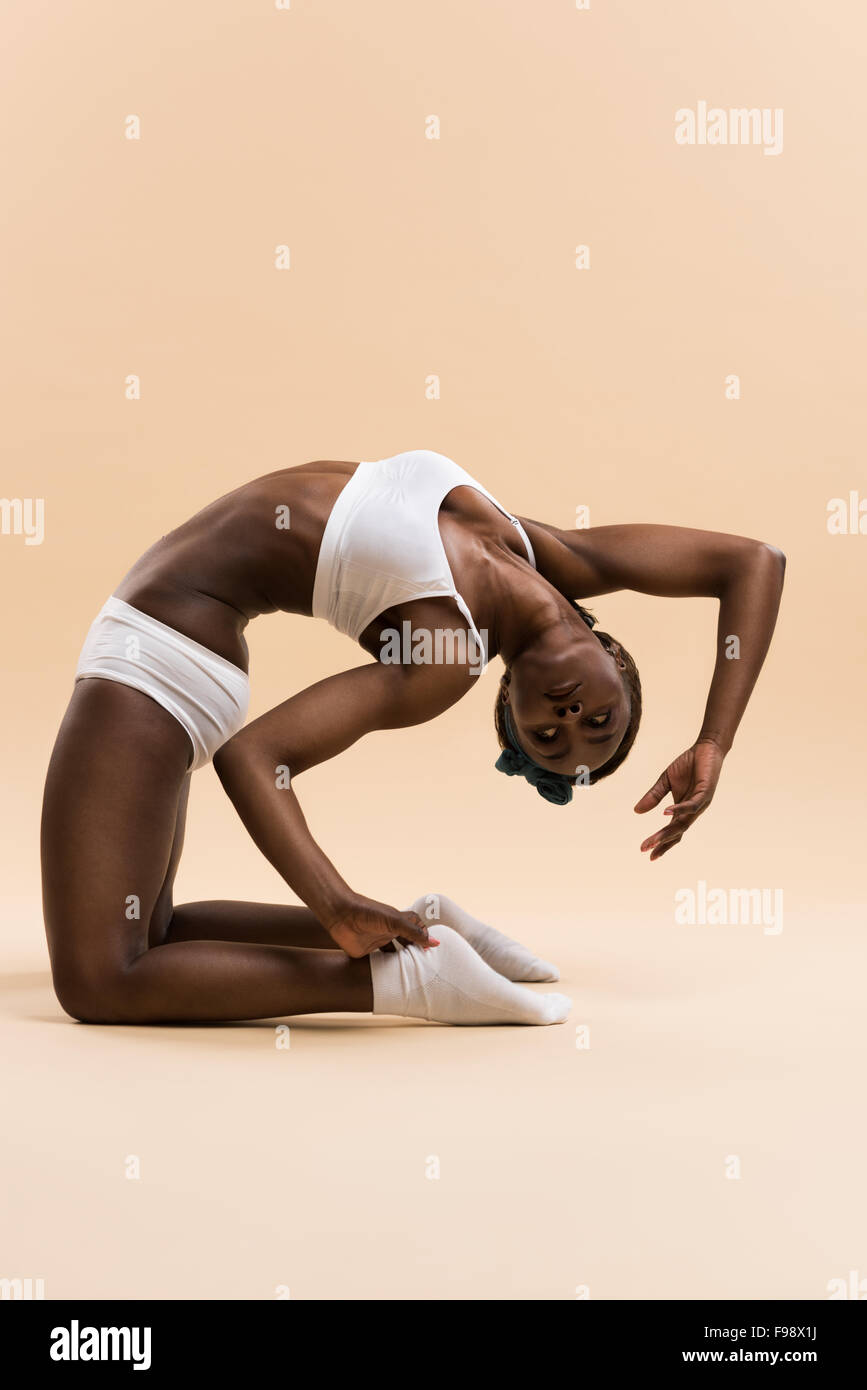 Portrait of young african woman doing stretching exercise on beige ...