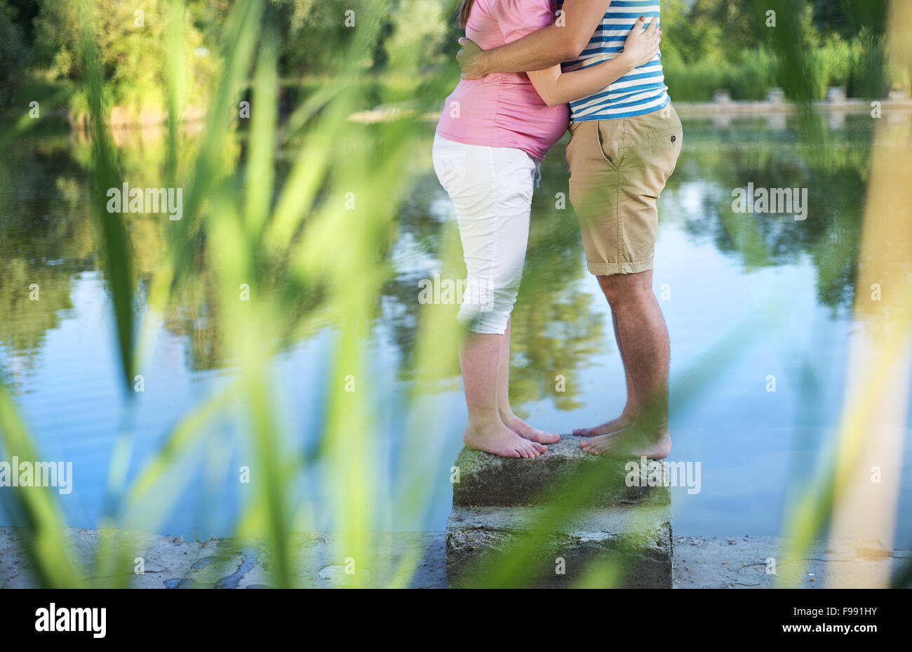 Happy young pregnant couple hugging by the lake Stock Photo - Alamy
