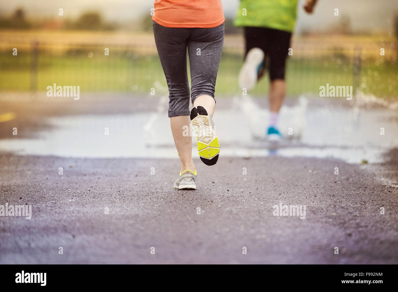Young couple running on asphalt sports field in rainy weather. Details