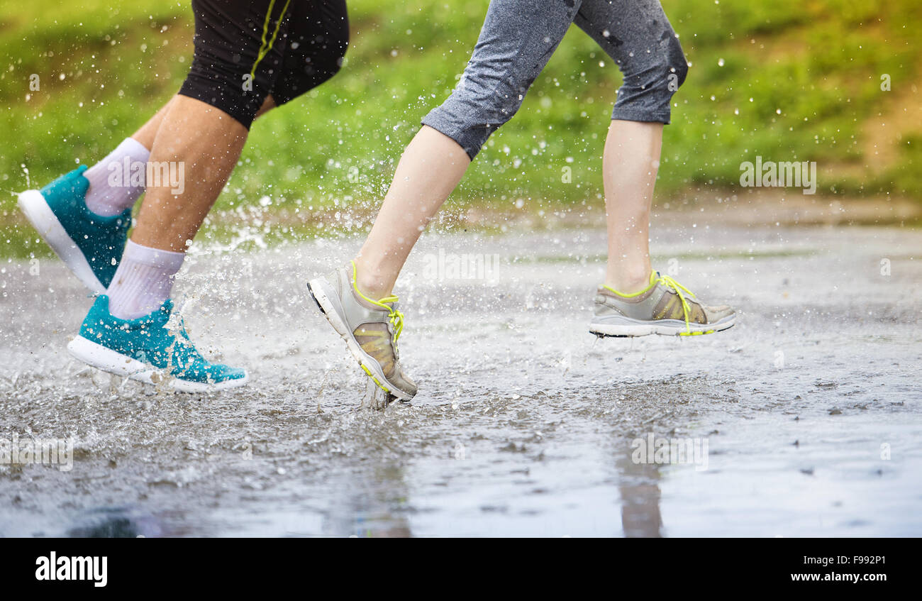 Young couple running on asphalt sports field in rainy weather. Details