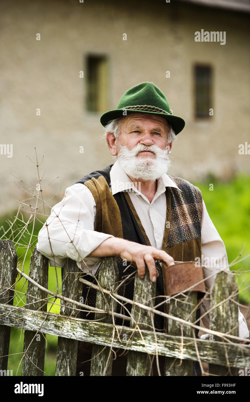 Old farmer with beard and hat standing by the lath fence with empty tins on top Stock Photo