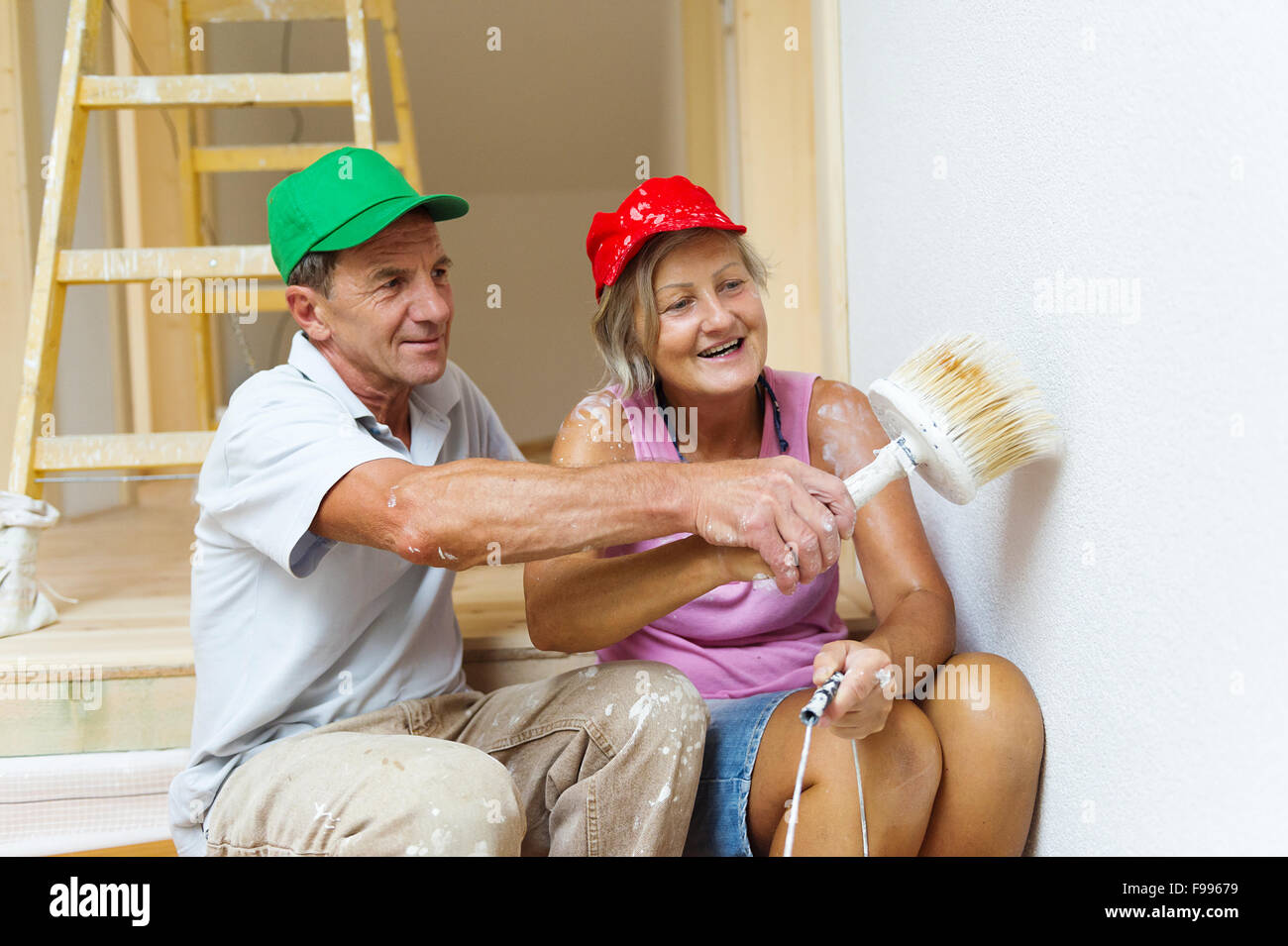 Active senior couple painting wall with brush in new house. They are having fun. Stock Photo