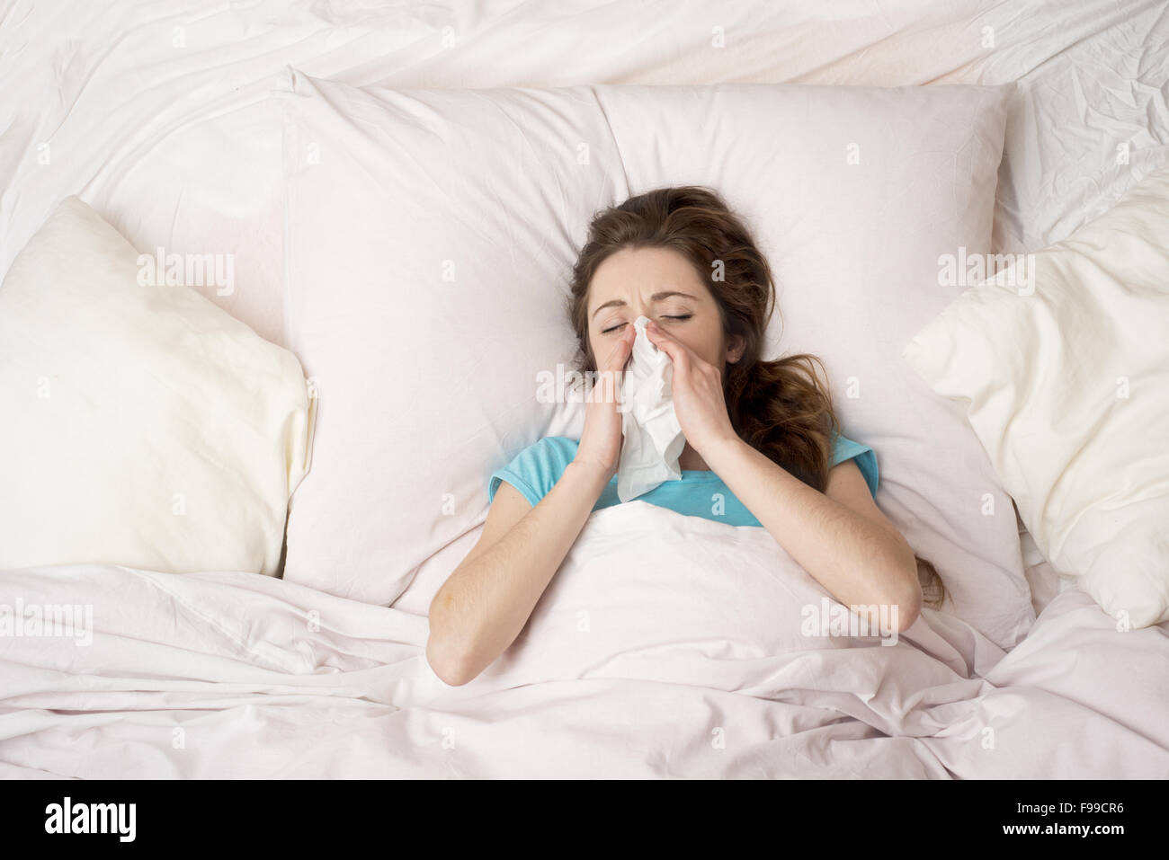 Sick woman lying in bed with high fever. She is blowing nose. Stock Photo