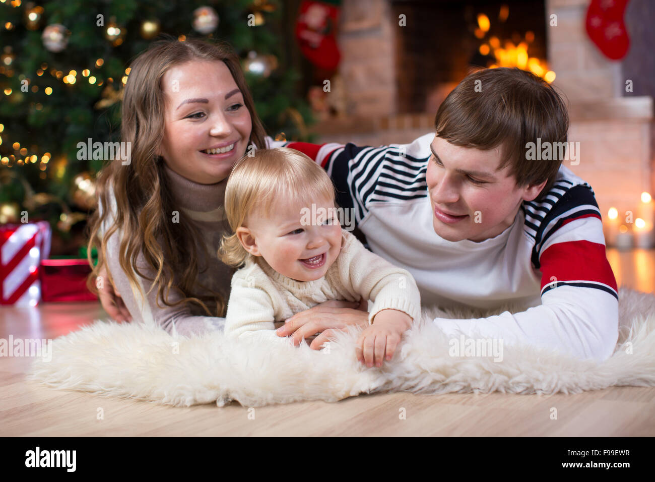 Happy young parents and child have a fun near Christmas tree at home.  Father, mother and son celebrating New Year together Stock Photo