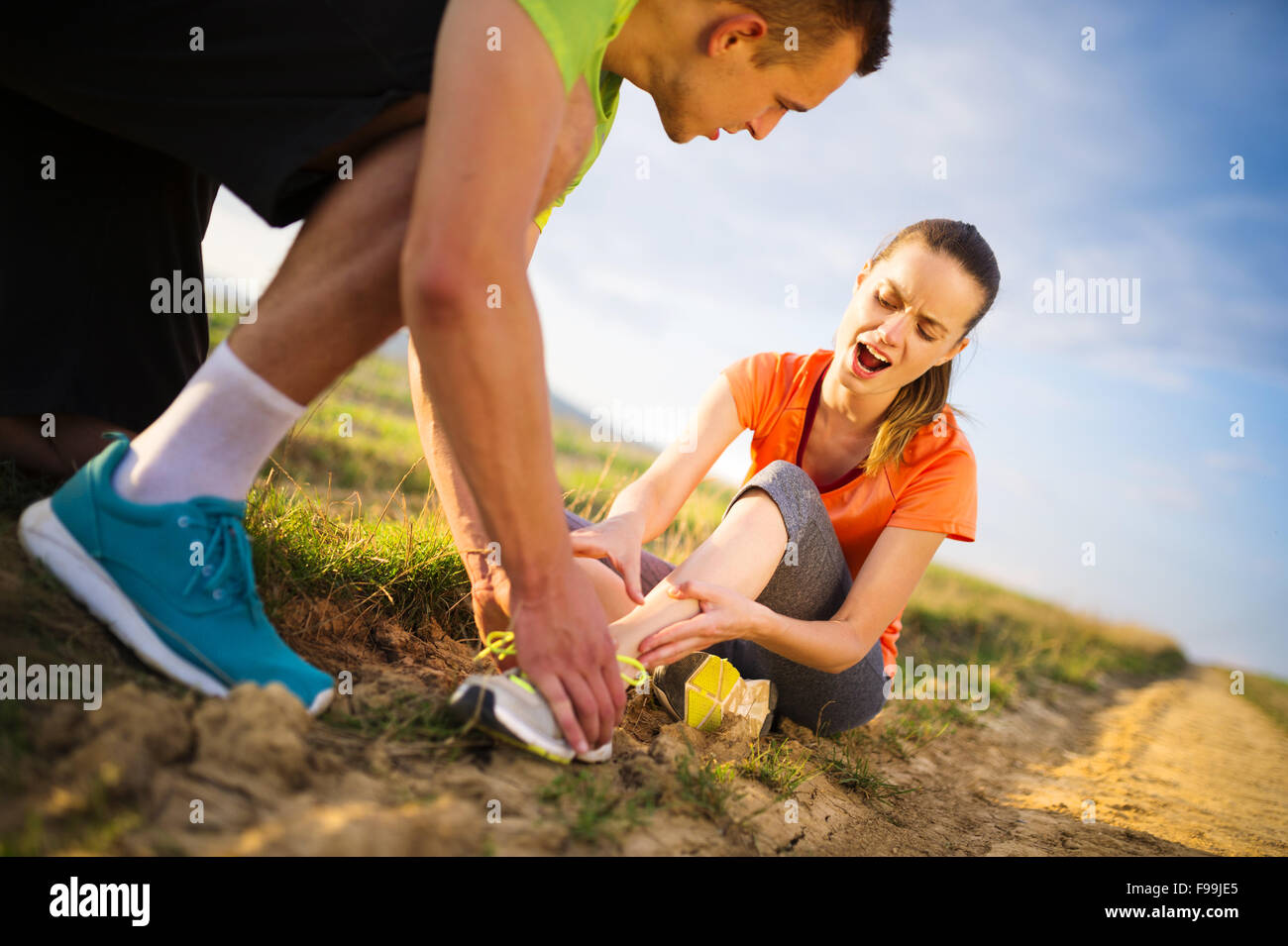Injury - sports woman with twisted sprained getting help from man touching her ankle. Stock Photo