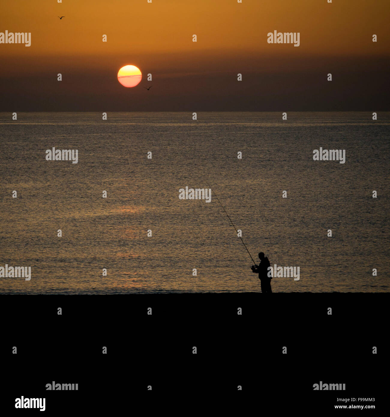 A fisherman prepares his fishing rod at Mediterranean sea as the sun rises in Barcelona coast. Stock Photo