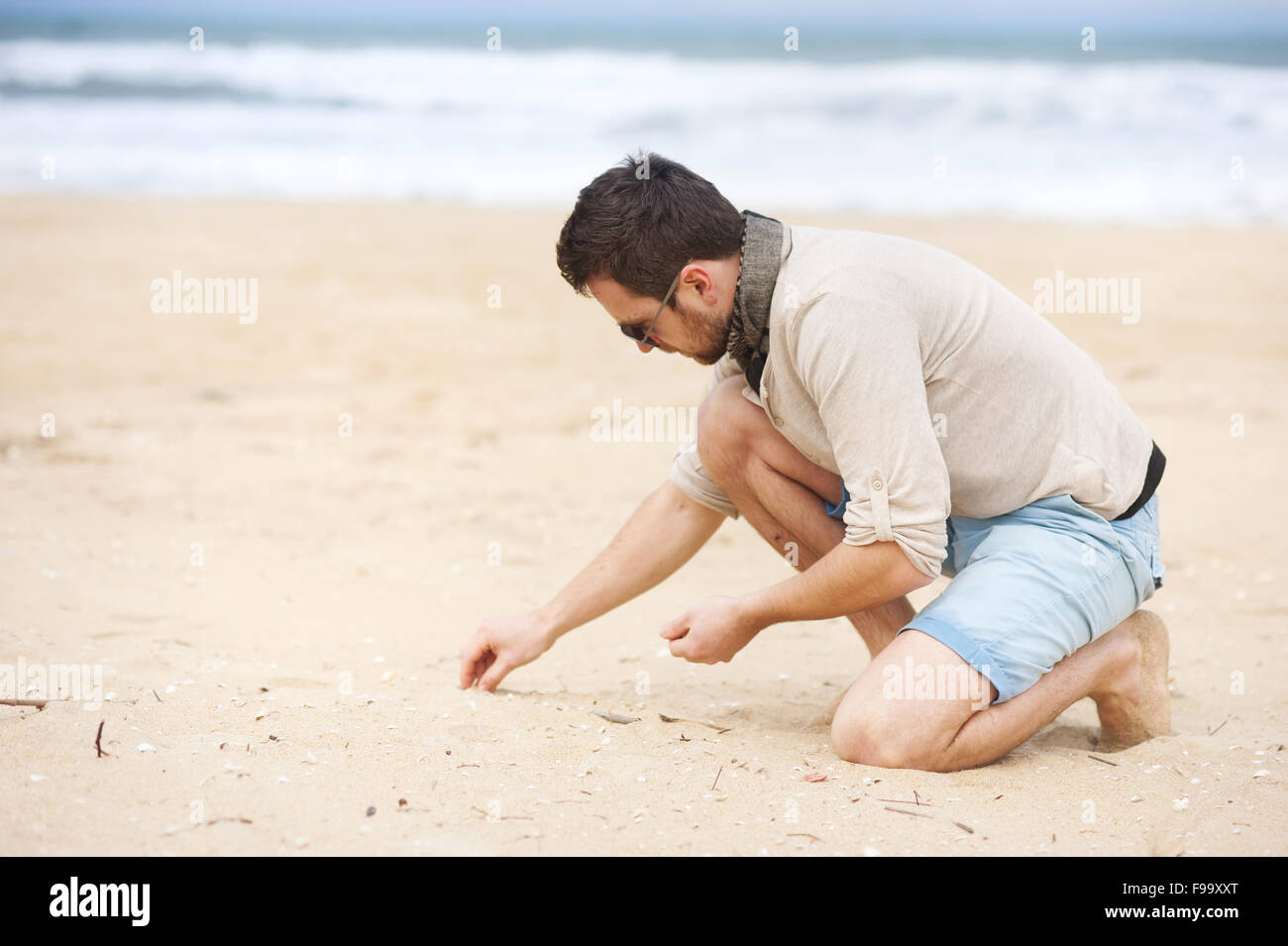Handsome man at the sunny beach collecting shells Stock Photo