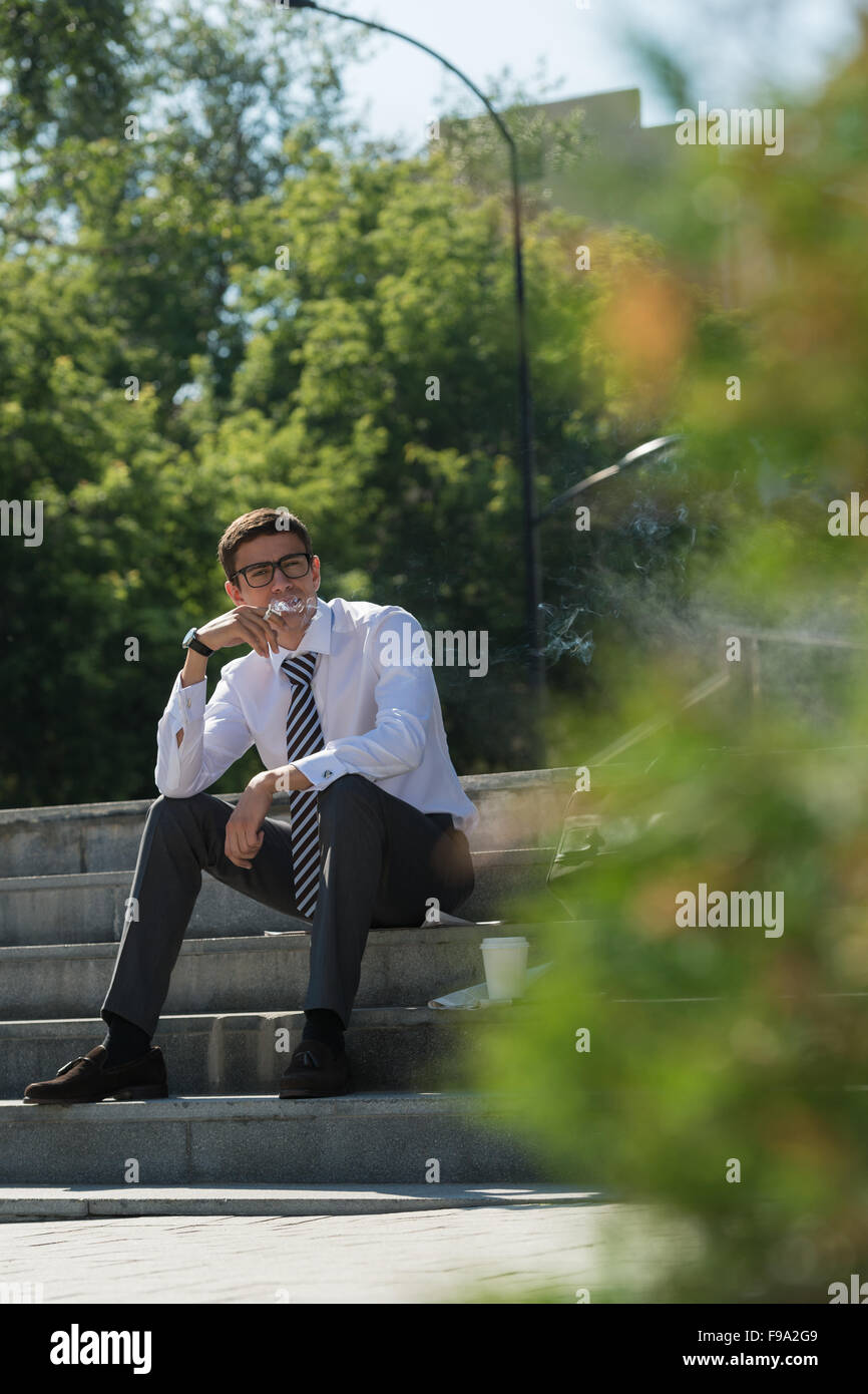 Well dressed business man smoking sitting on a street sidewalk Stock Photo