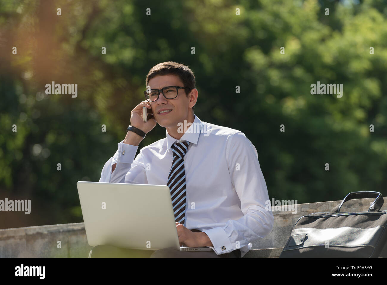 Man with laptop calling by phone at summer park on bright day Stock Photo