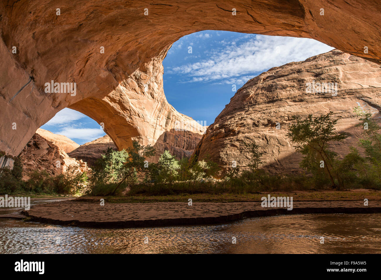 A large natural arch spans over a canyon with running water in the desert. Stock Photo