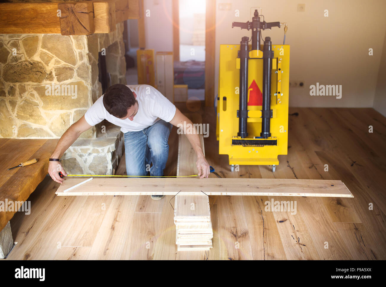 Young handyman installing and measuring plywood for wooden floor Stock Photo