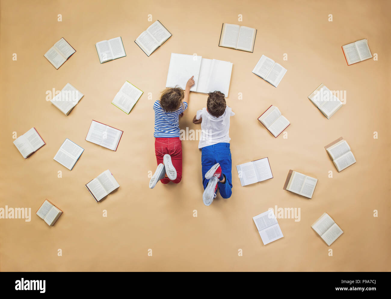 Happy children are reading book on the floor with group of books around them Stock Photo