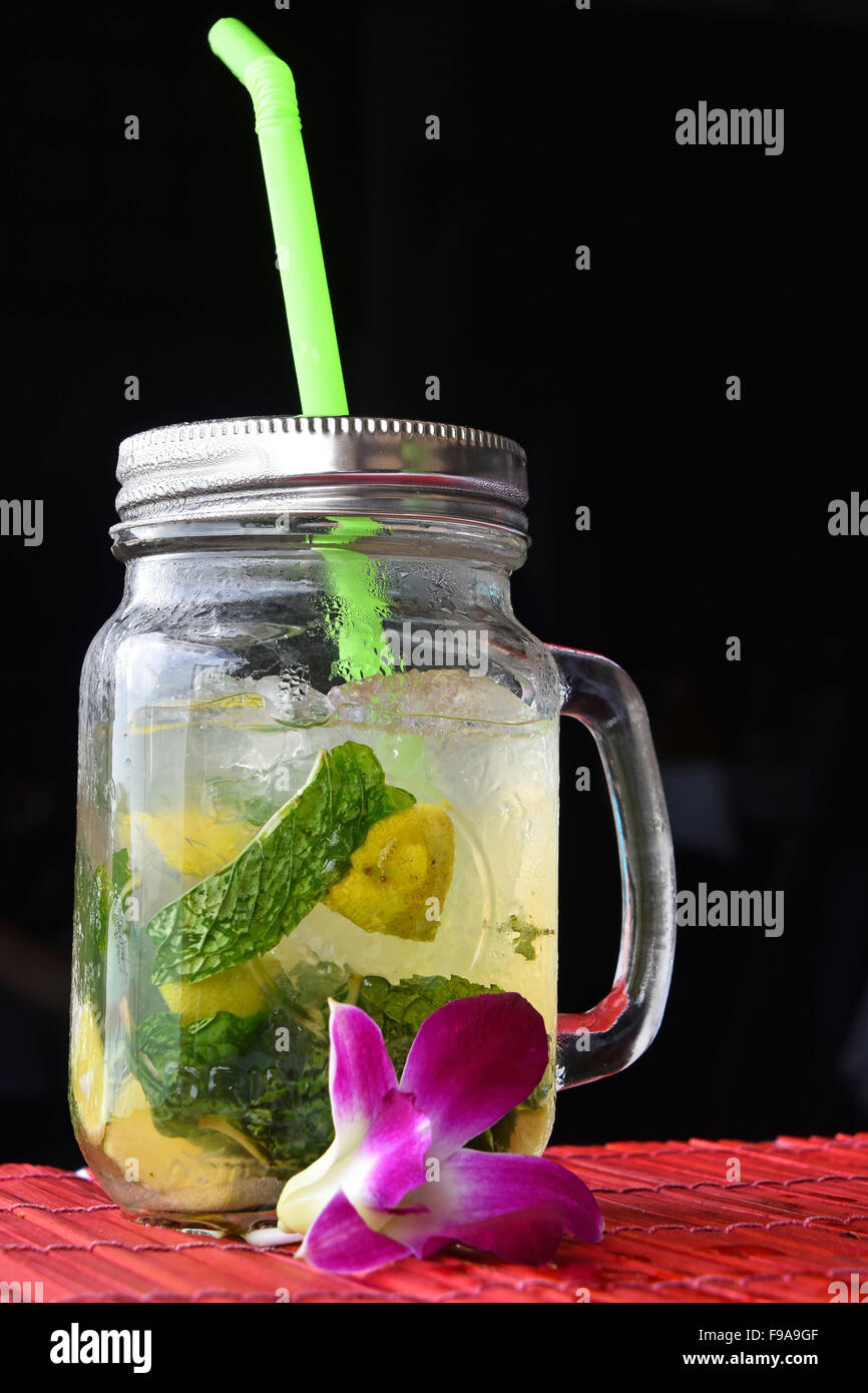 Big jars mug style full glass of fresh frozen mojito with metal cap lid, straw and purple orchid flower in cafe with black backg Stock Photo