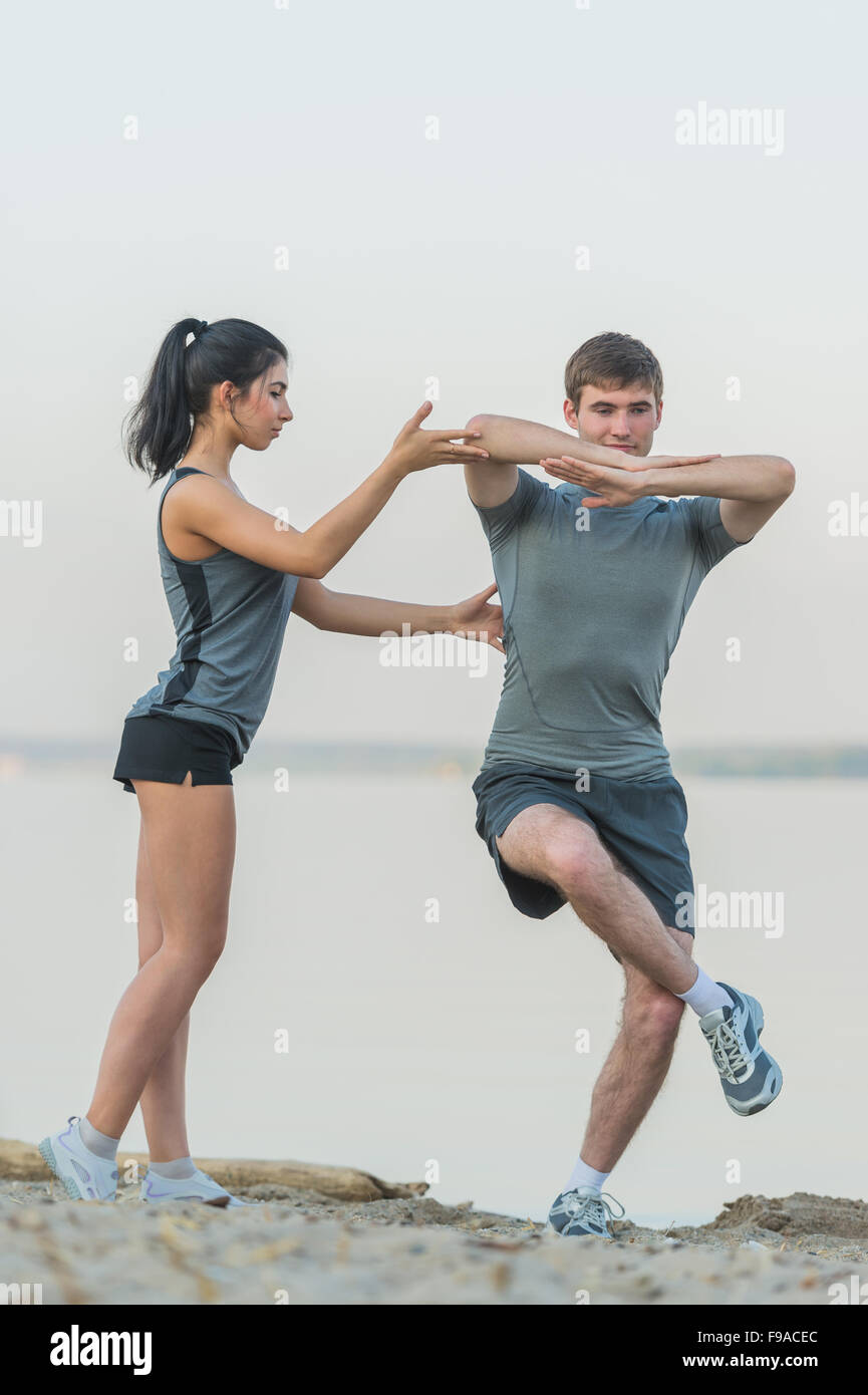Fitness, sport, friendship and lifestyle concept - smiling couple making stretching yoga exercises on beach at morning Stock Photo