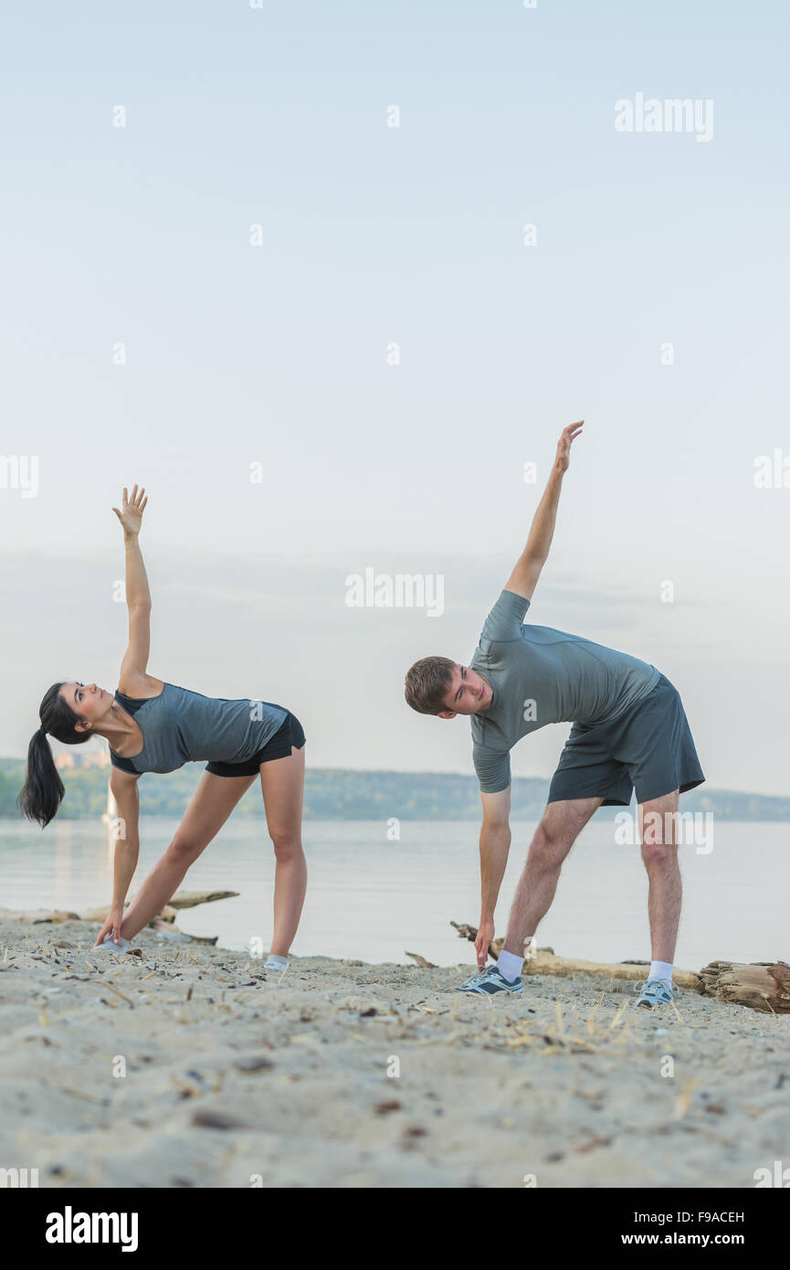 Fitness, sport, friendship and lifestyle concept - smiling couple making stretching yoga exercises on beach at morning Stock Photo