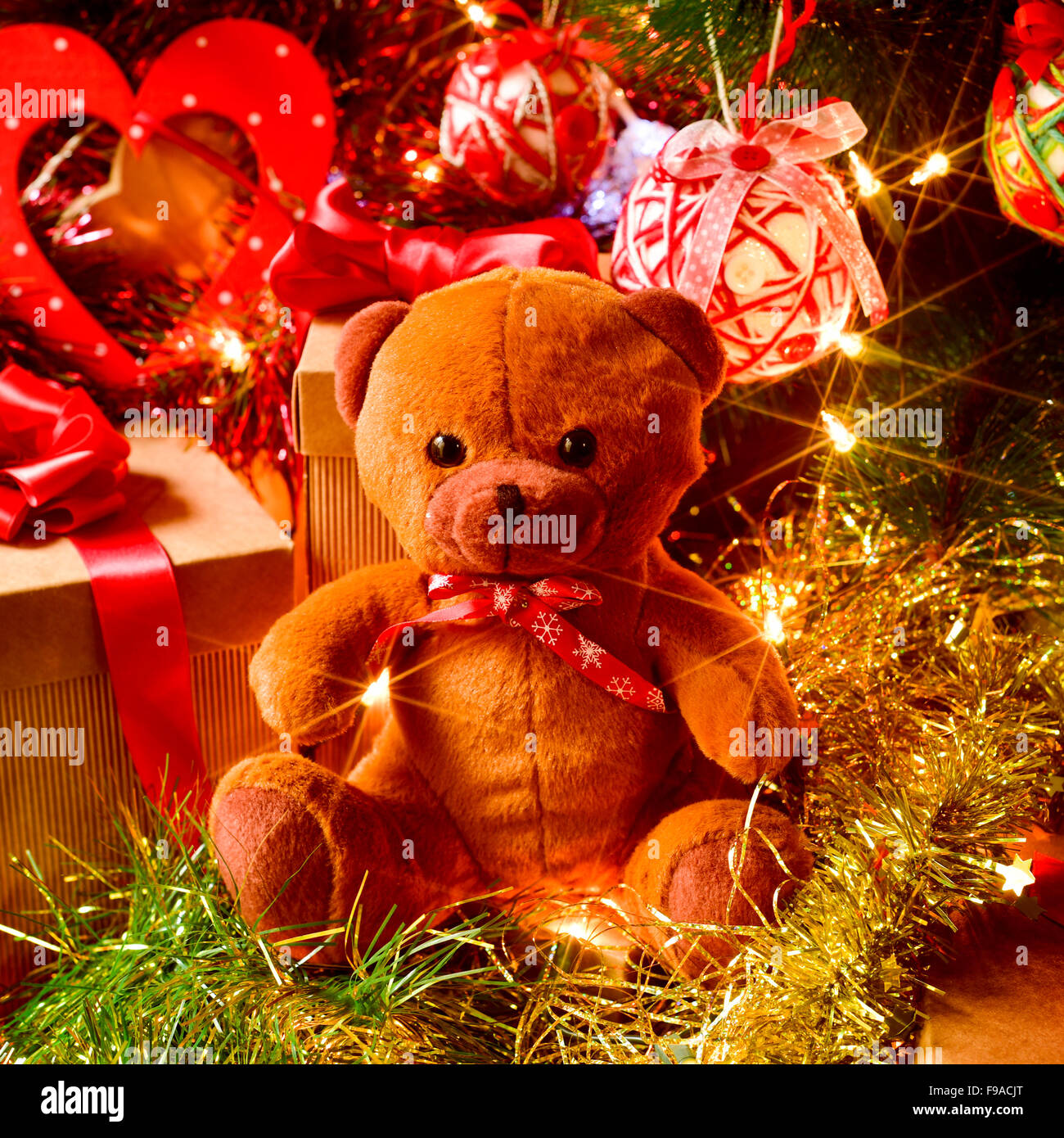 closeup of a brown teddy bear and some gifts under a christmas tree ornamented with lights, balls and tinsel Stock Photo