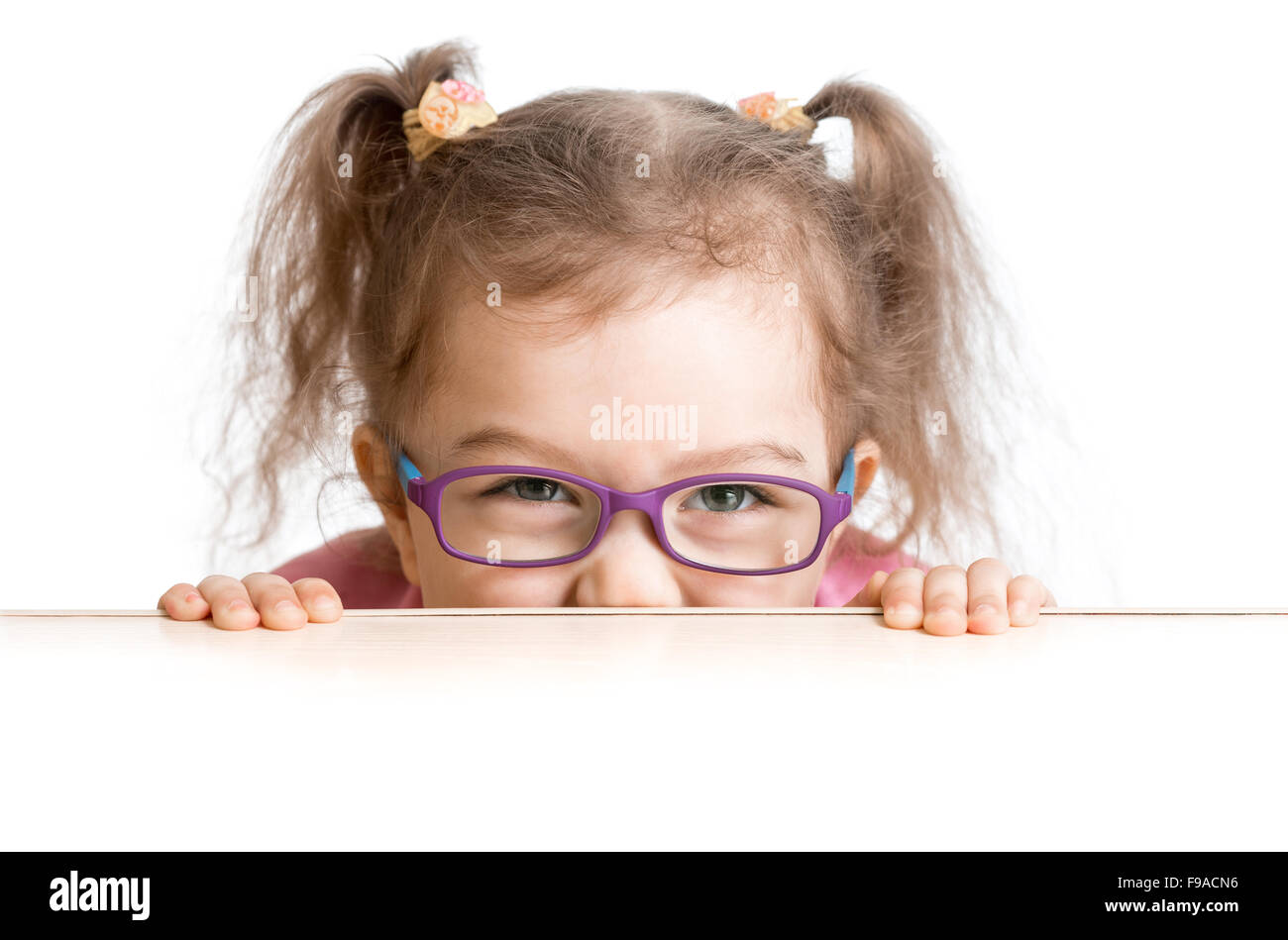 frightened kid in spectacles looking from under table desk Stock Photo