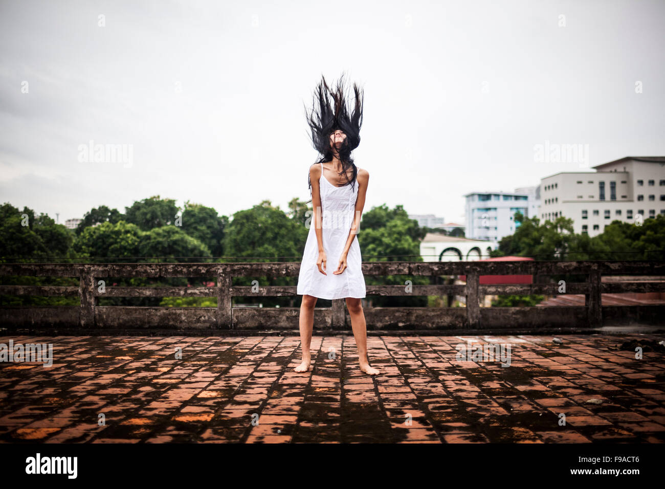A young Vietnamese woman flips her hair back on an old factory rooftop in Hanoi, Vietnam. Stock Photo
