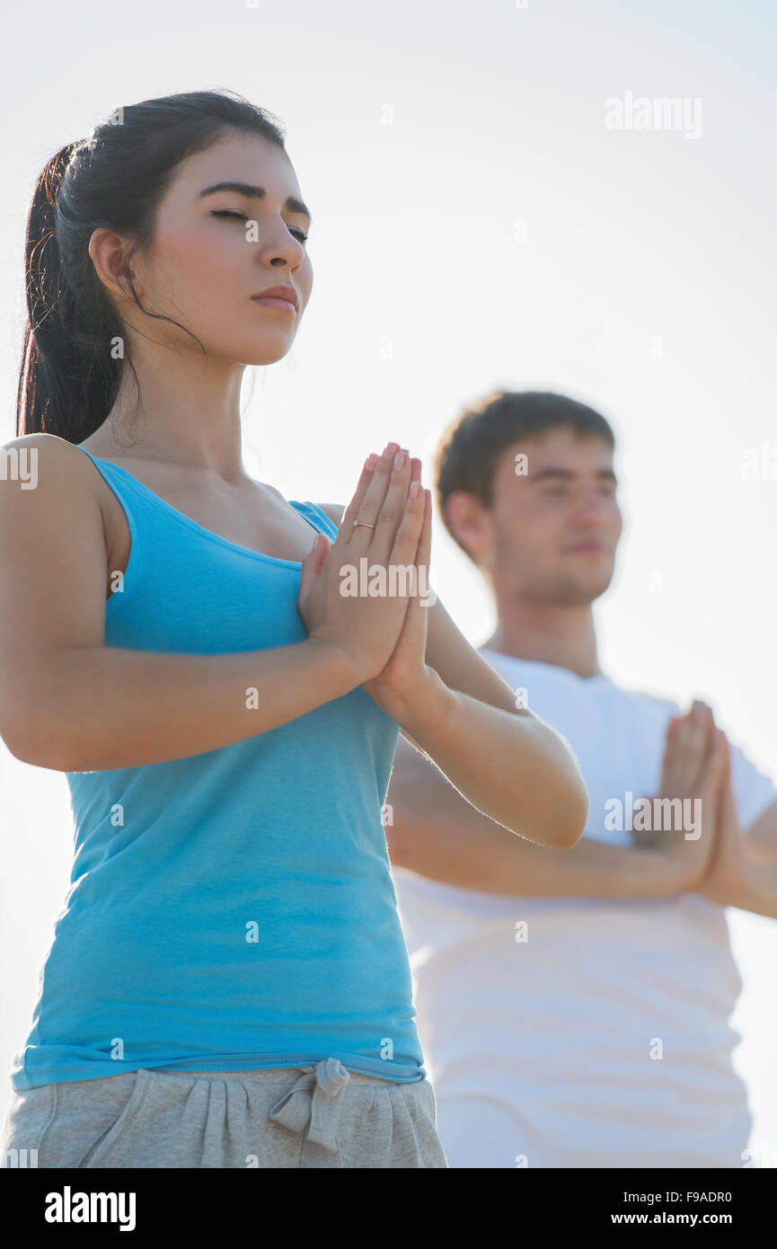 Fitness, sport, friendship and lifestyle concept - smiling couple making meditation yoga exercises on beach at morning Stock Photo