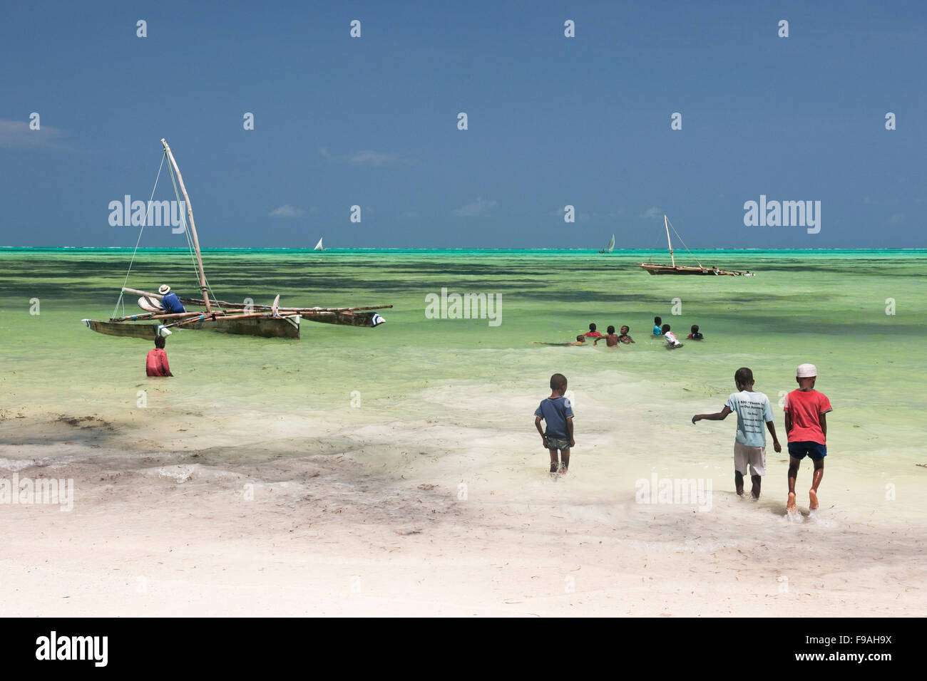 Children watch and play during the annual Dhow race in Jambiani Zanzibar with blue sky and blue sea and white sand Stock Photo
